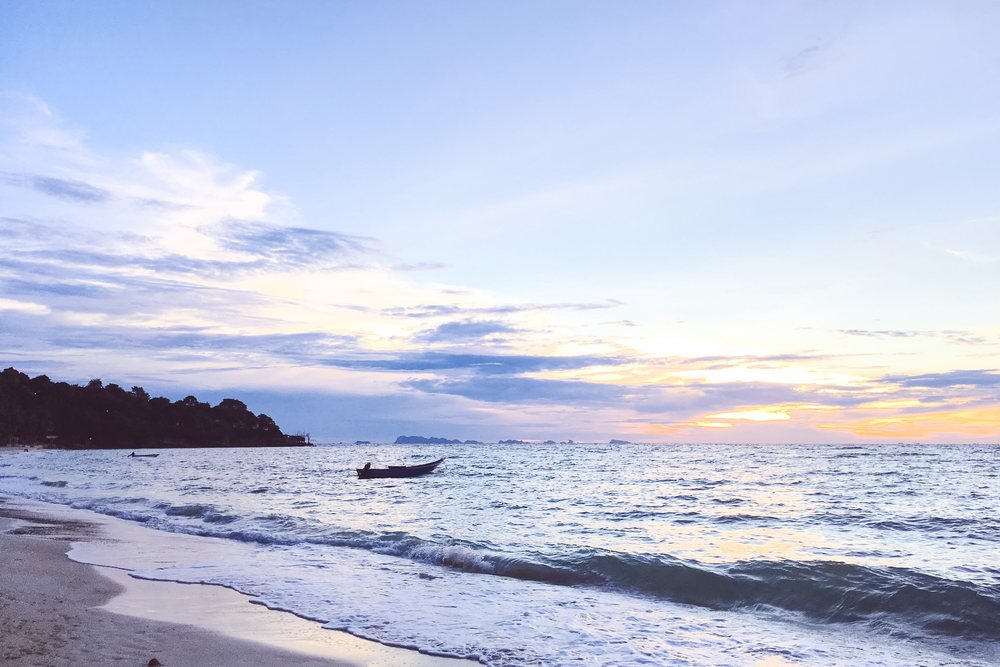 Ocean waves and boats on a sandy beach at sunset in the Philippines