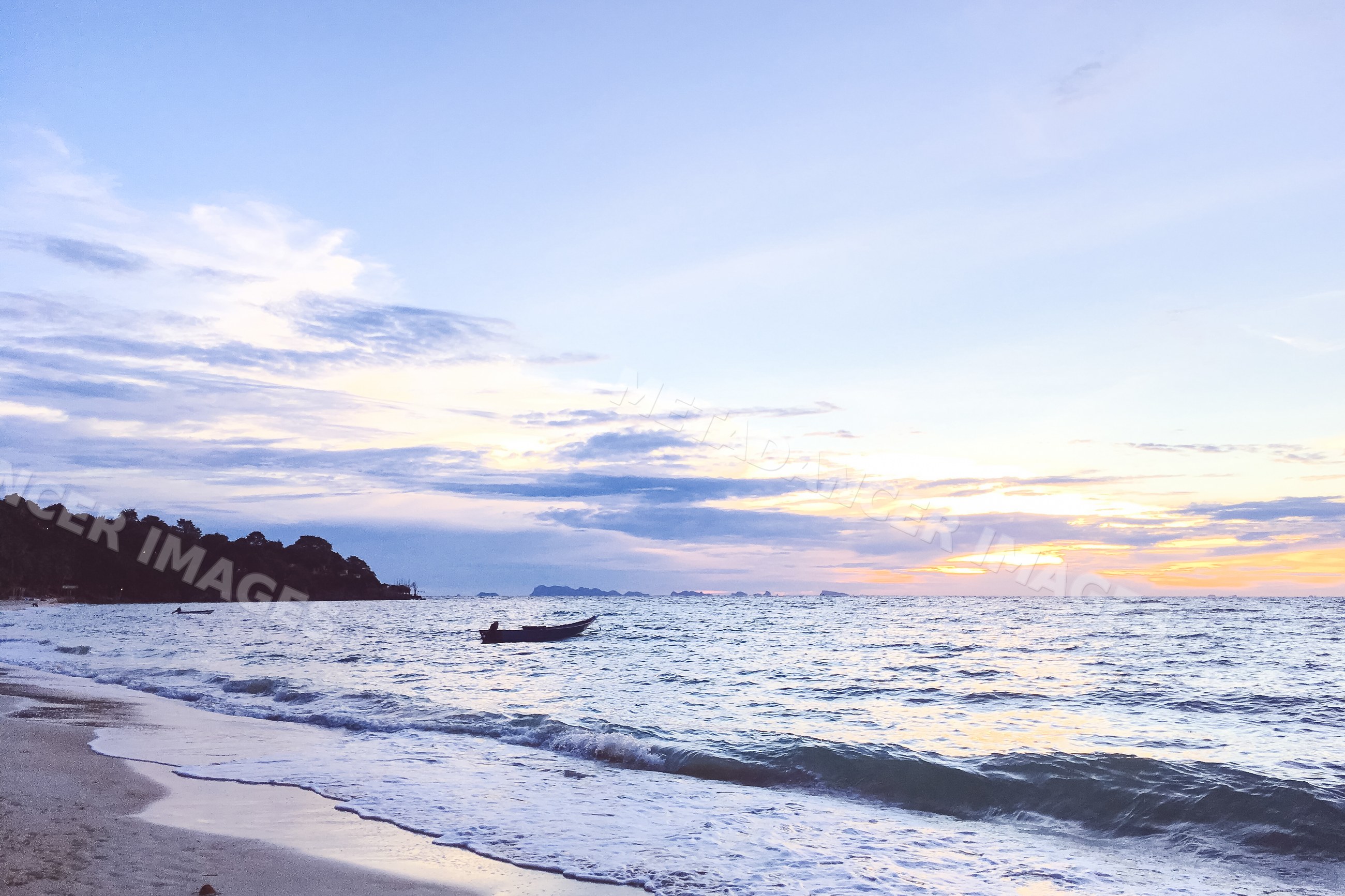 Ocean waves and boats on a sandy beach at sunset in the Philippines