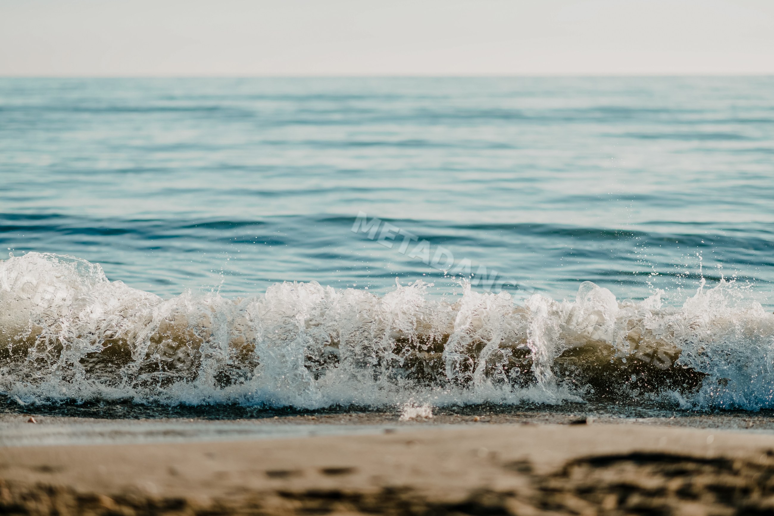 Ocean wave breaking on sandy beach under clear sky in a beach
