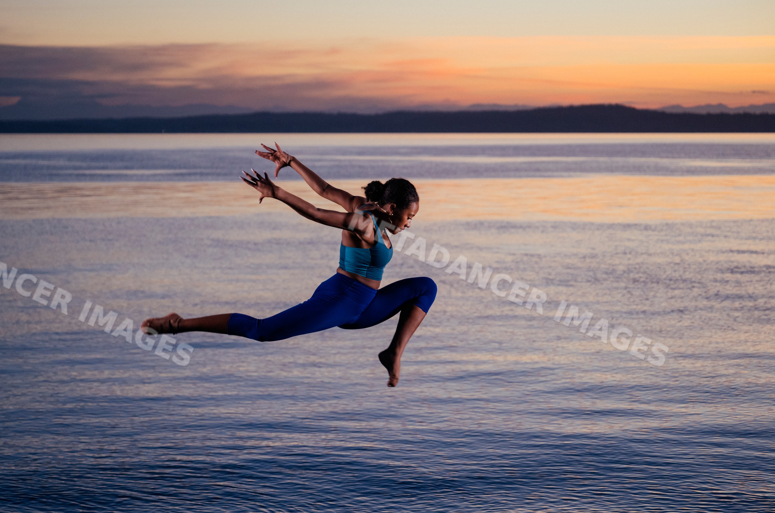 Hispanic woman performing yoga acrobatic leap over ocean water