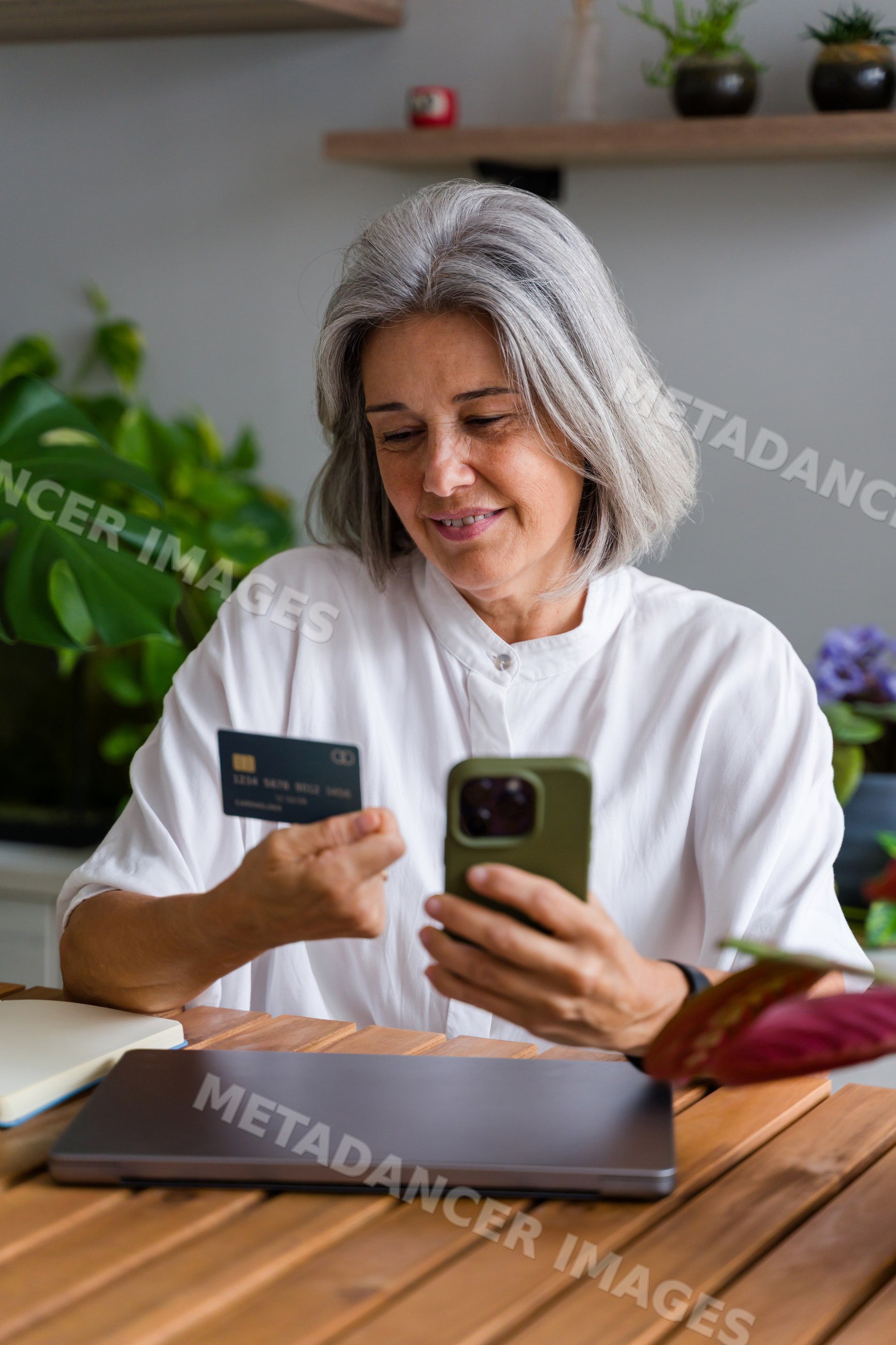 Mature white woman using smartphone and card for online shopping