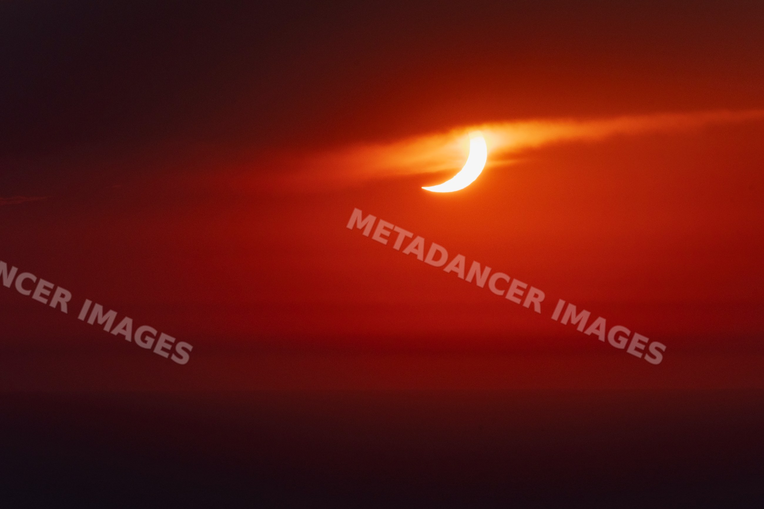 Solar eclipse crescent emerging through clouds over valldemossa