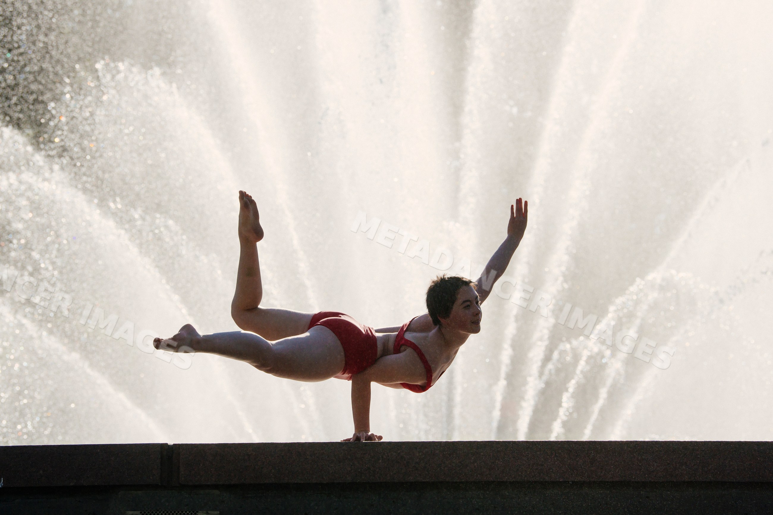 White woman performing handstand balancing pose by a water fountain