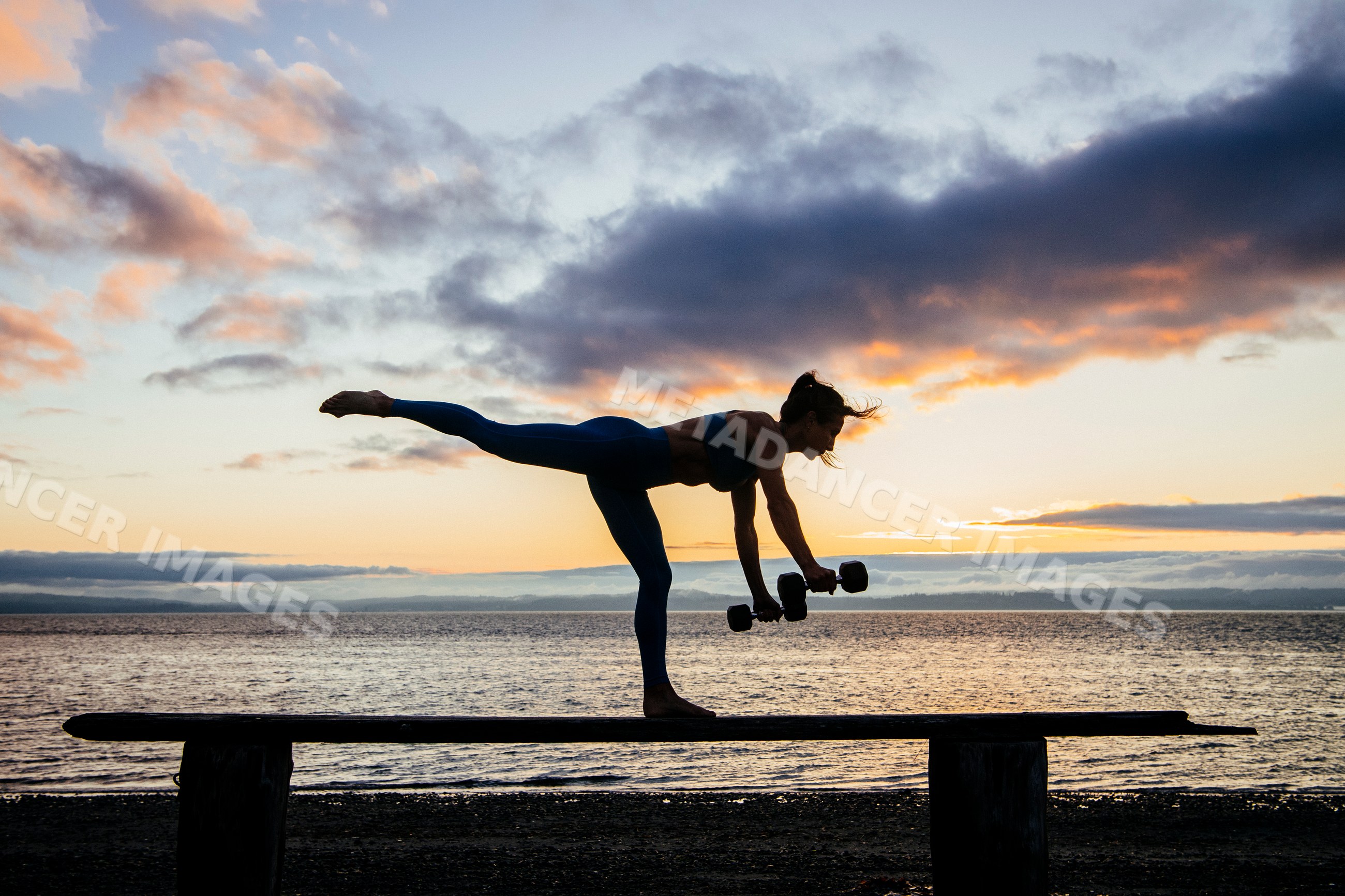 White woman balancing and exercising with dumbbells on a beam at beach
