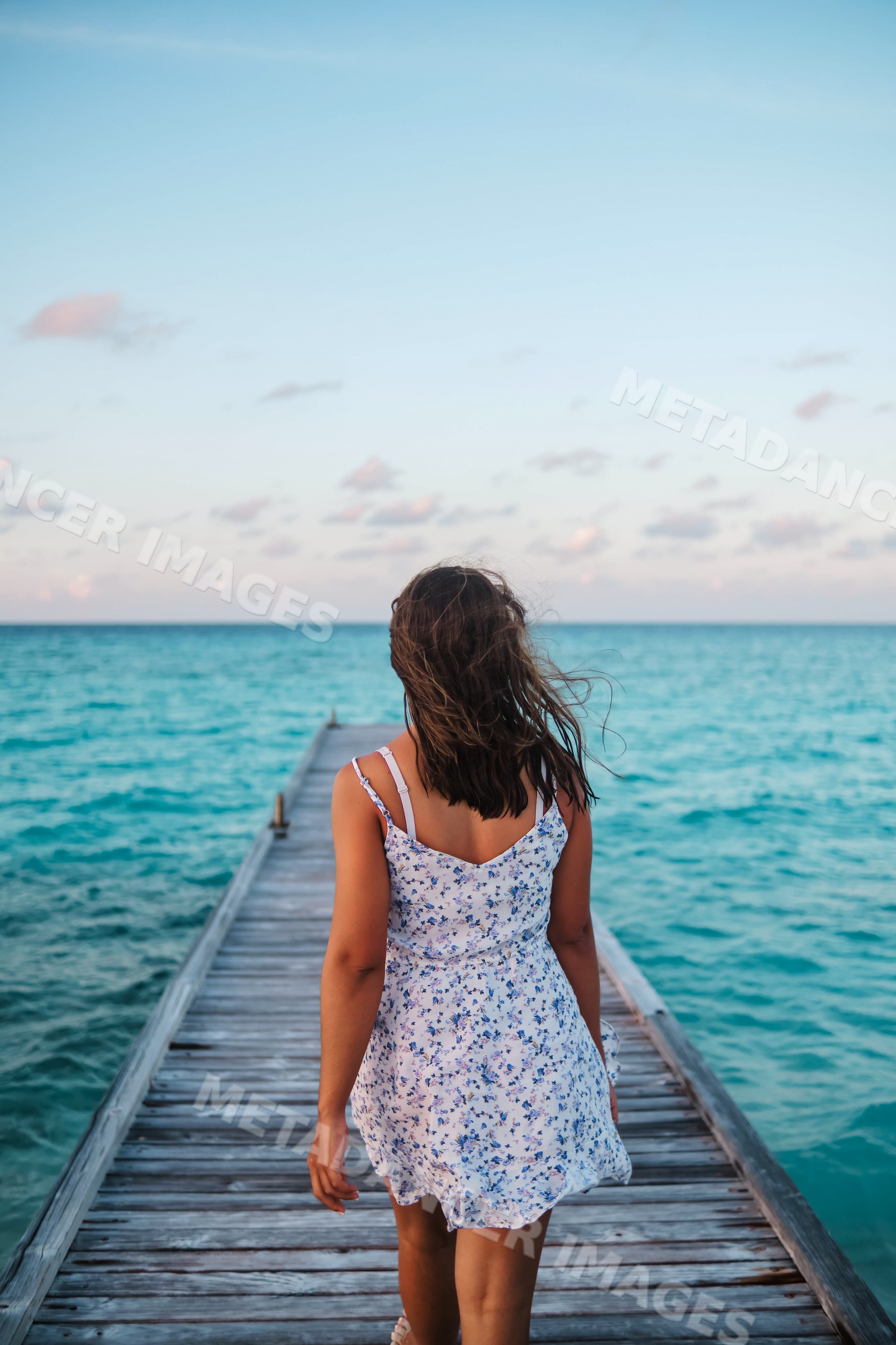 A white woman walks on a wooden pier toward the ocean