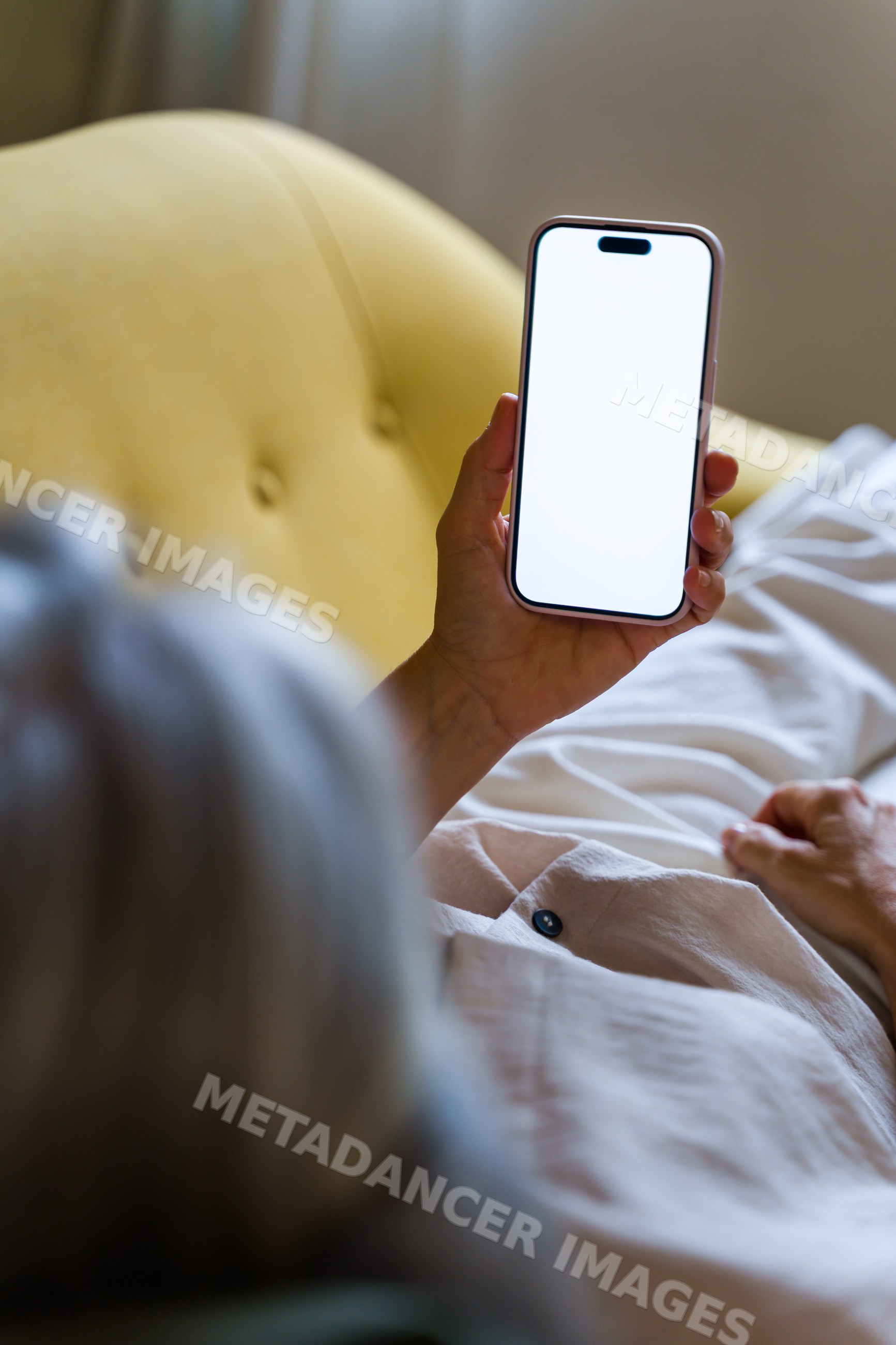 White person holding smartphone with blank screen on bed indoors