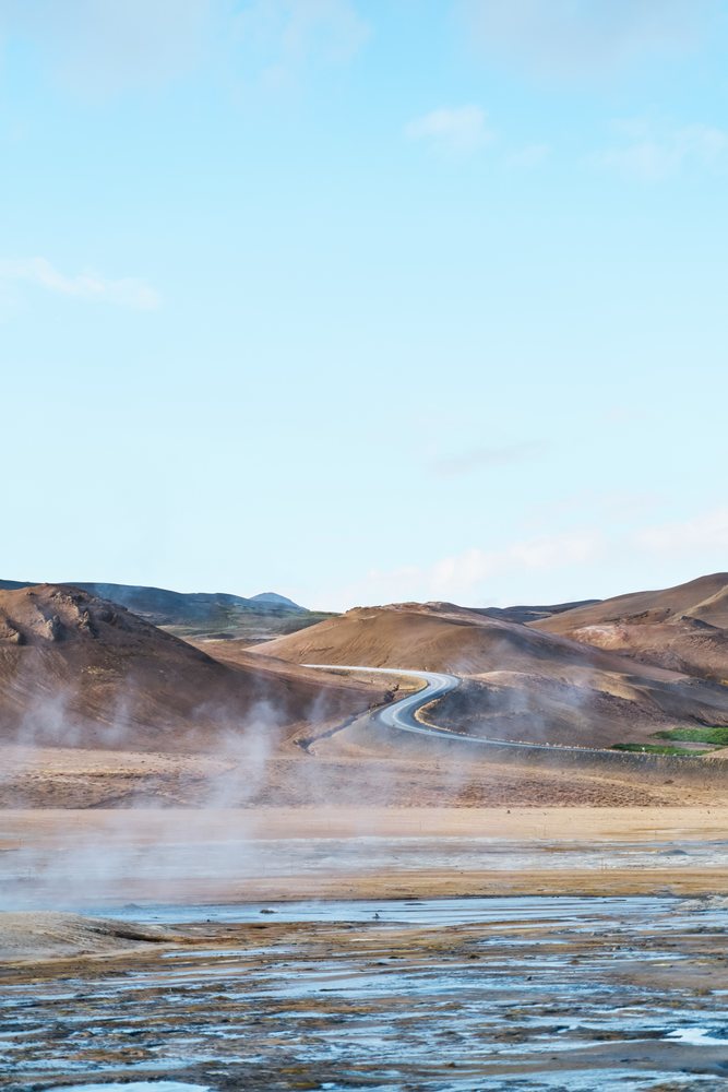 Steam rises from a geothermal area with a winding road