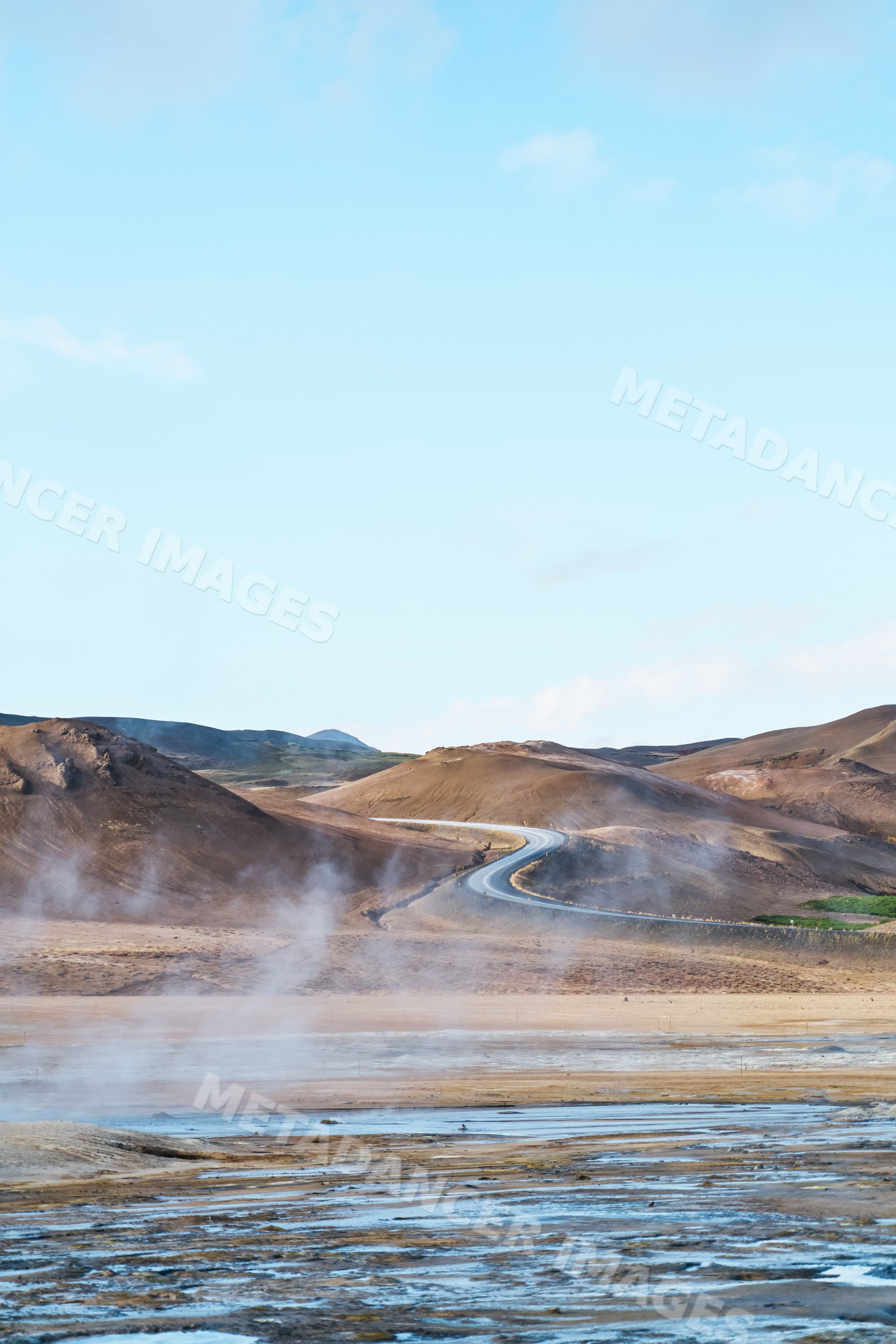Steam rises from a geothermal area with a winding road