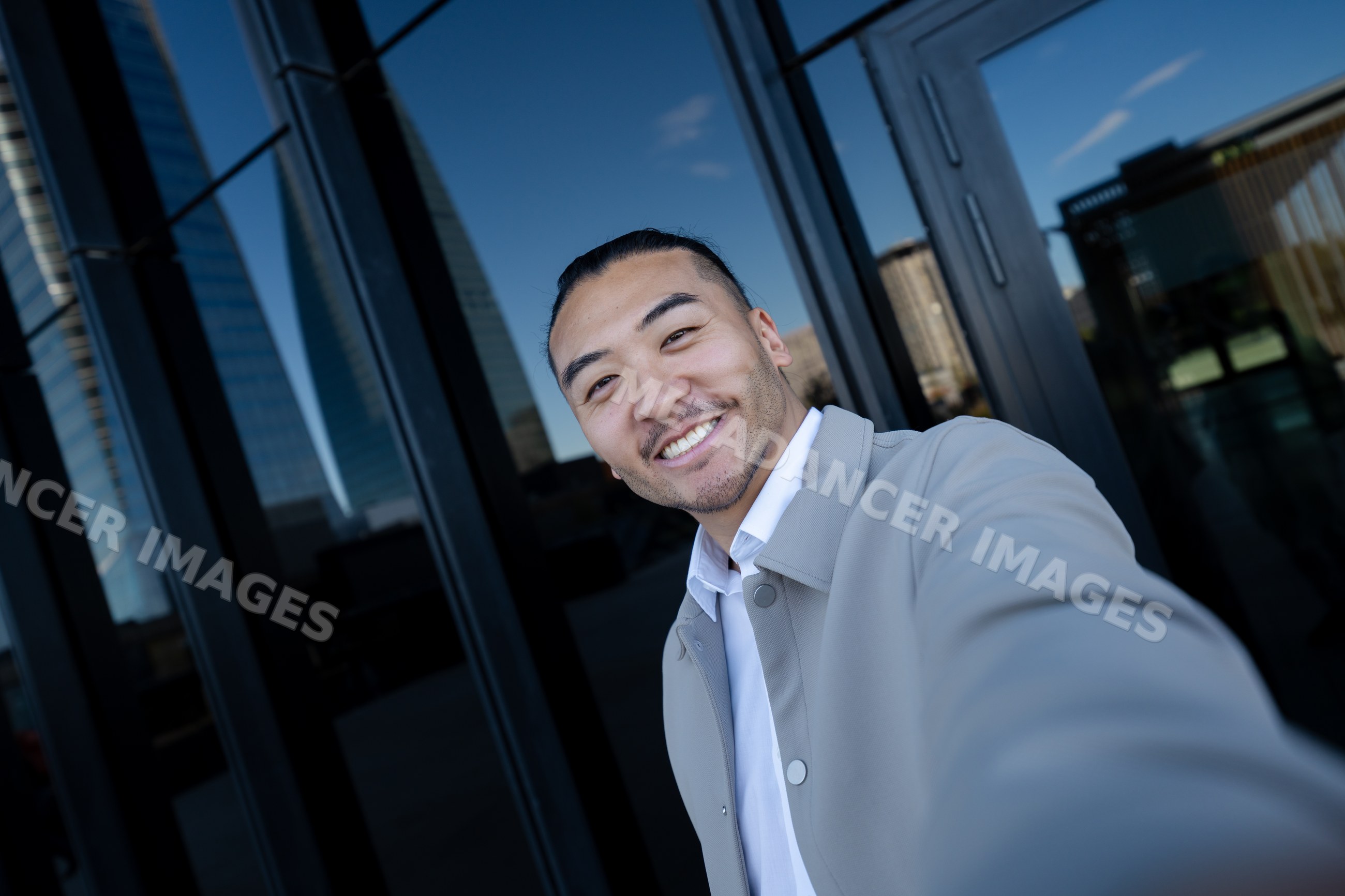 Man taking a selfie in urban area with glass building reflections