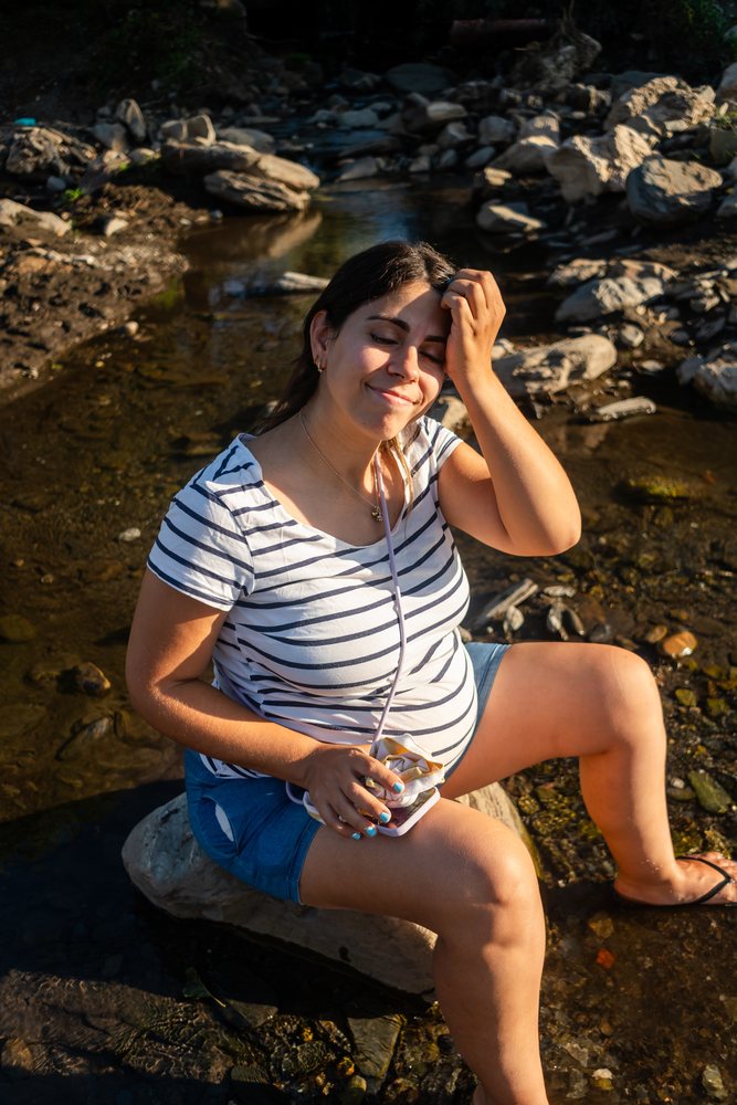 Pregnant woman relaxes by a rocky riverbank enjoying warm sunlight
