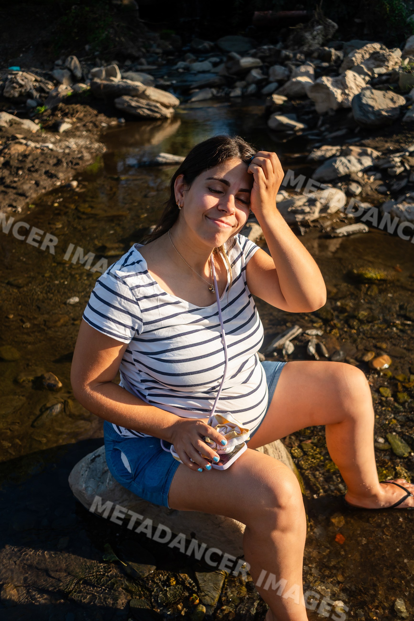 Pregnant woman relaxes by a rocky riverbank enjoying warm sunlight