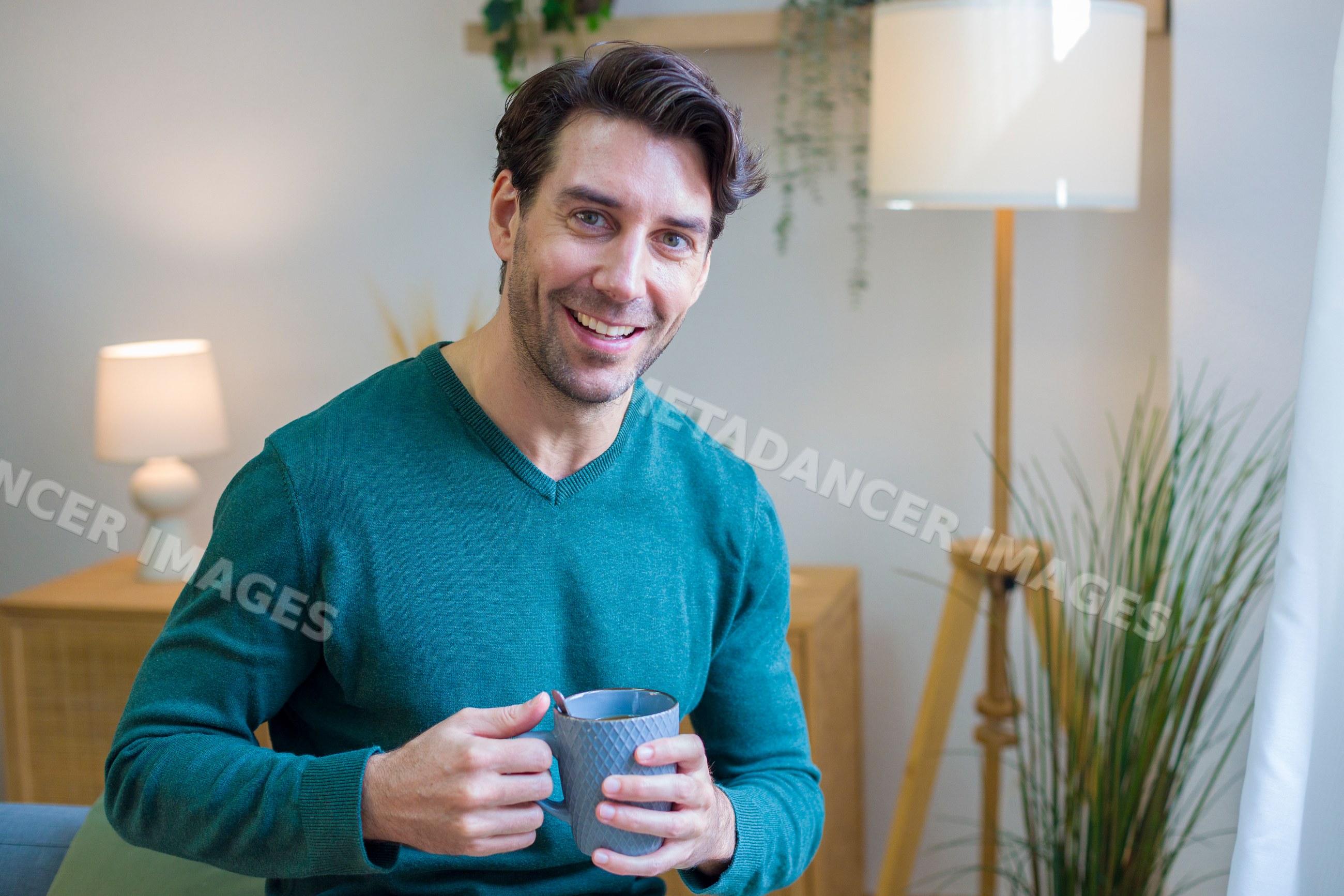 White man holding coffee cup smiling in cozy home interior