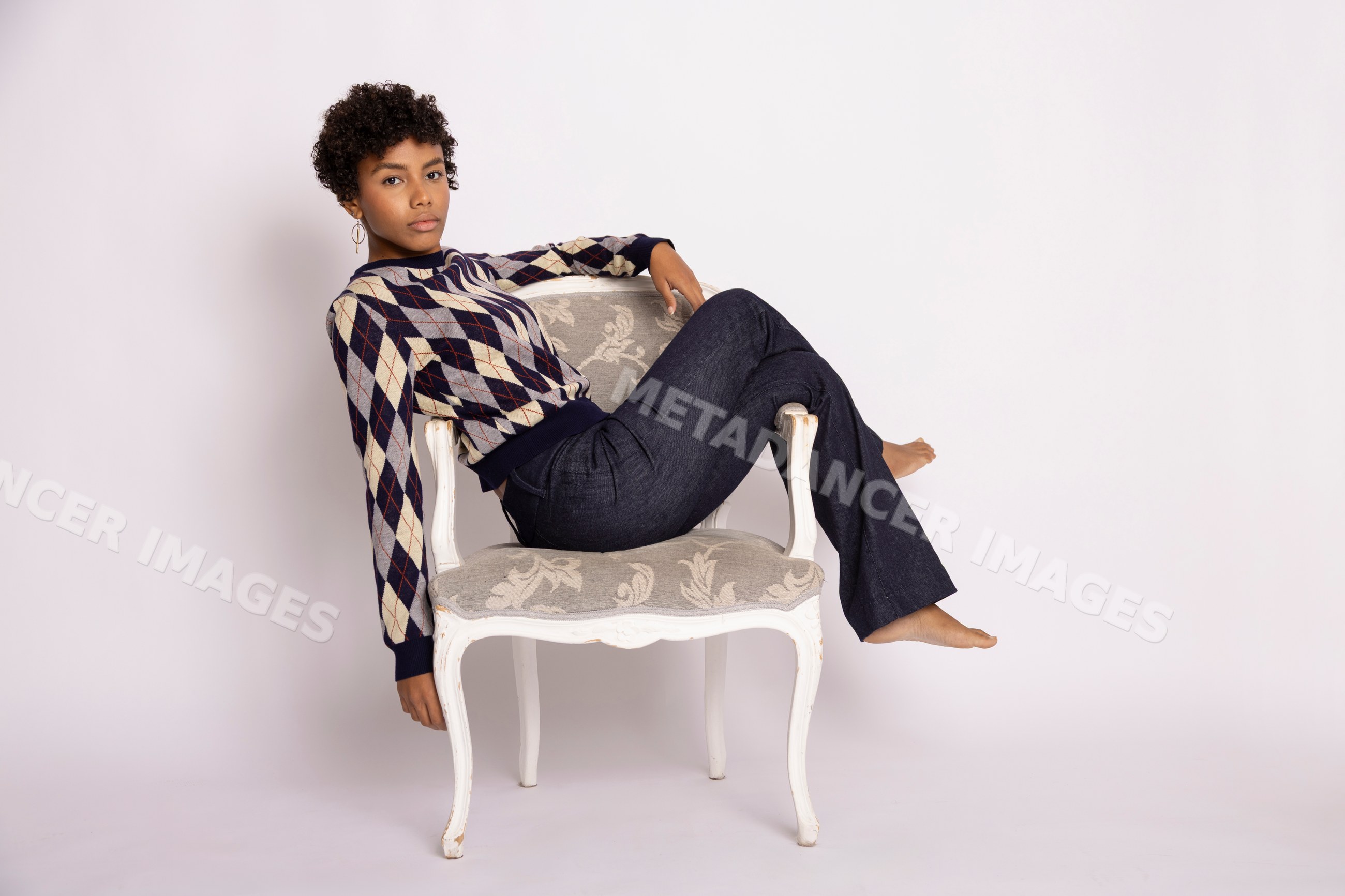 Young Hispanic woman in argyle sweater sitting on ornate armchair