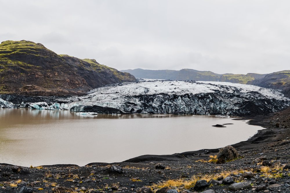 A glacier front melting into a lake amid volcanic terrain