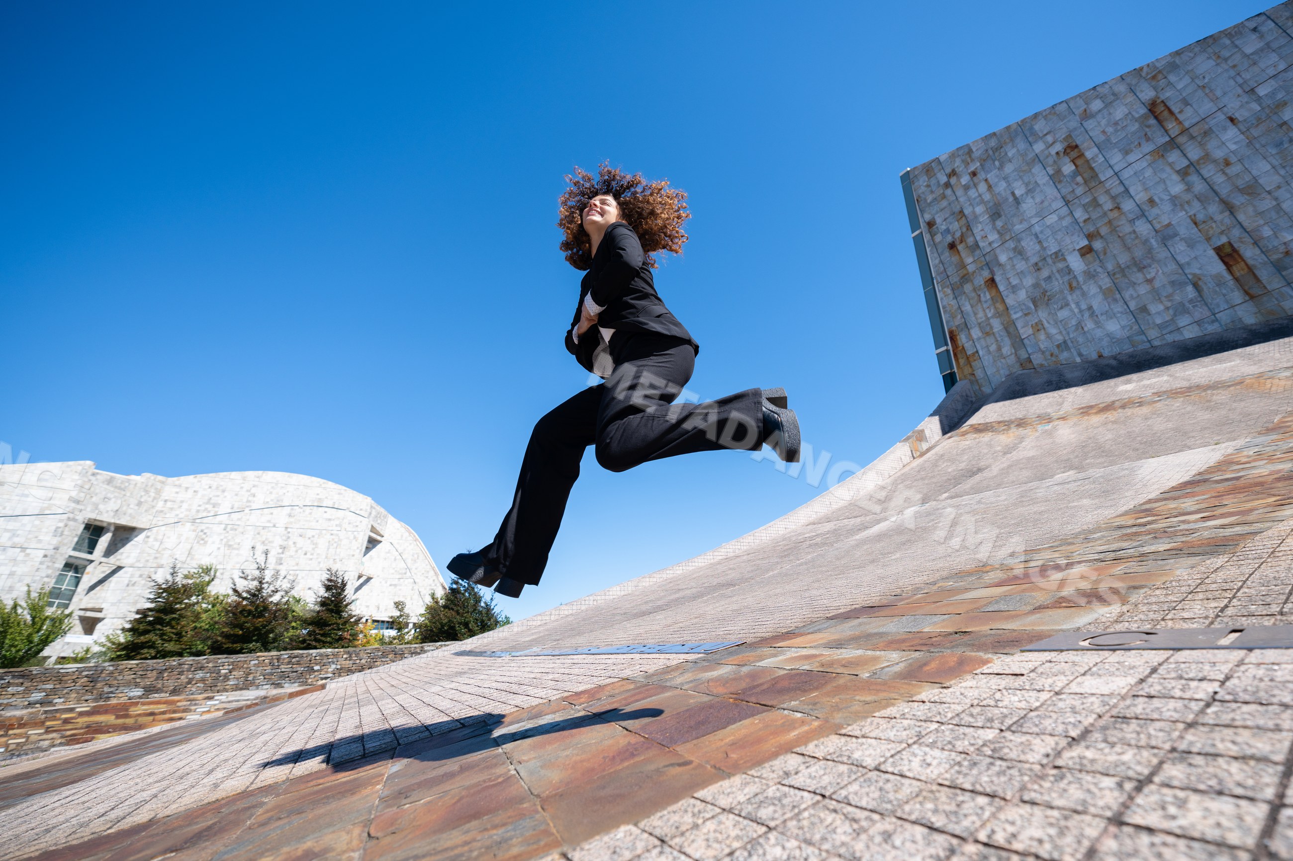 White woman jumping near modern curved concrete wall