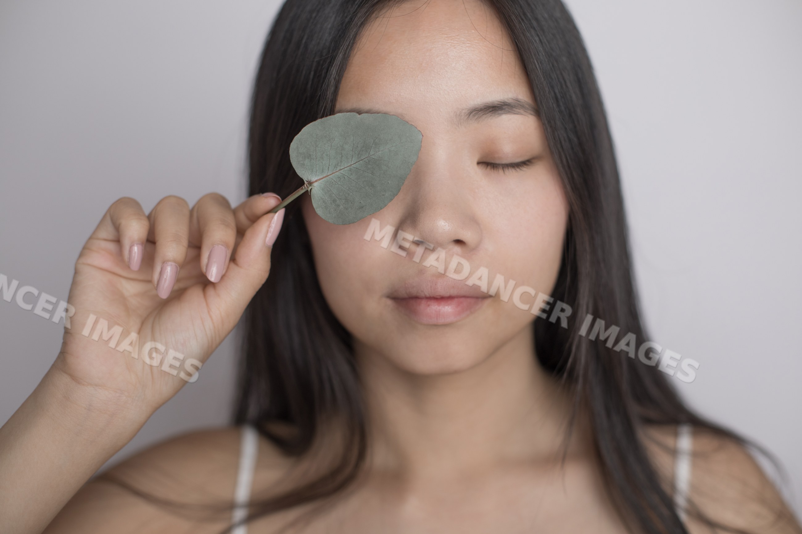 Southeast Asian woman holding green leaf over her closed eye
