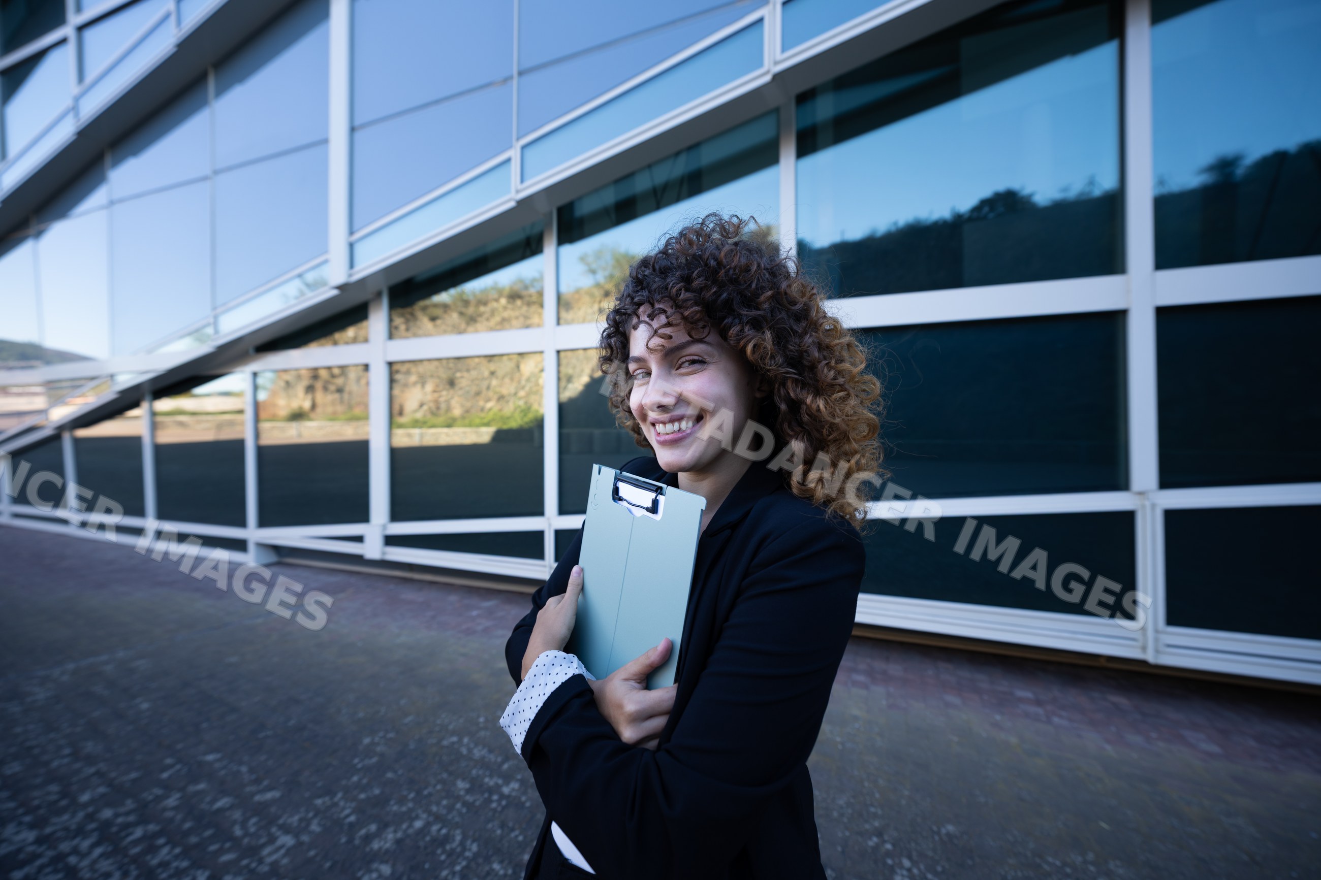 Businesswoman holding clipboard smiling outside modern glass building