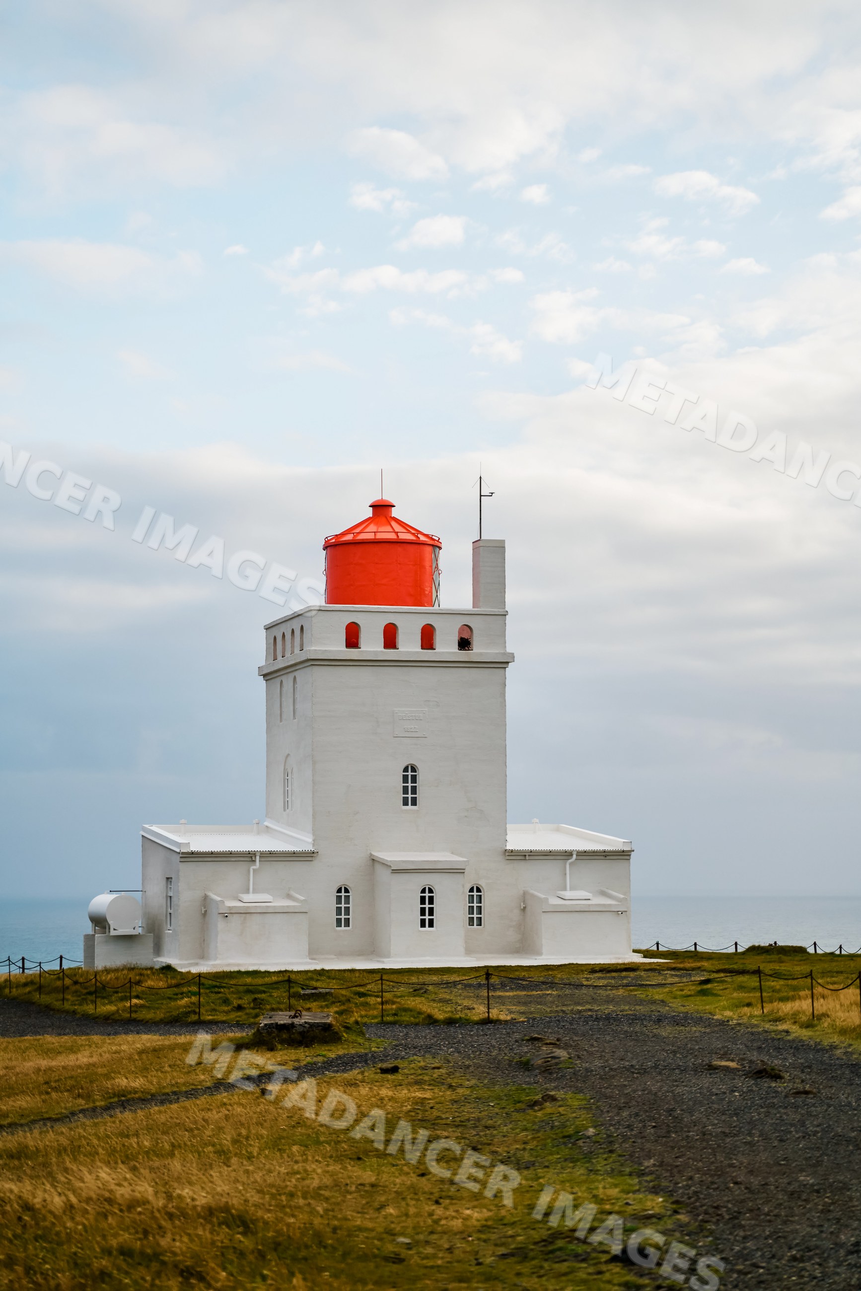 A white lighthouse with a red roof on the coast of Iceland