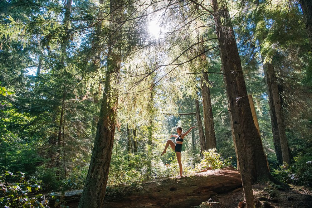 Contortionist white woman balancing on log in sunlit forest