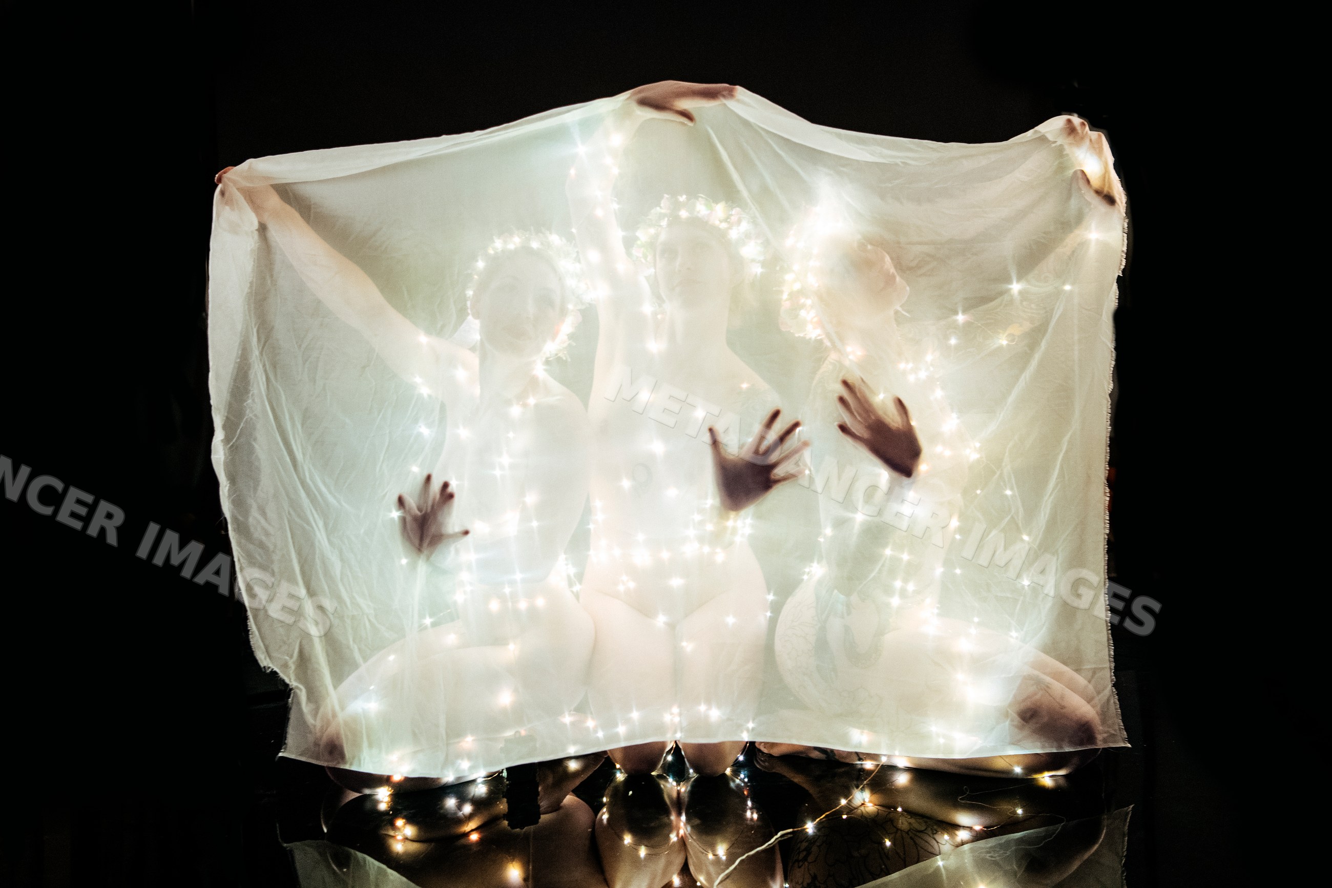 Three white women with glowing fairy lights behind a veil