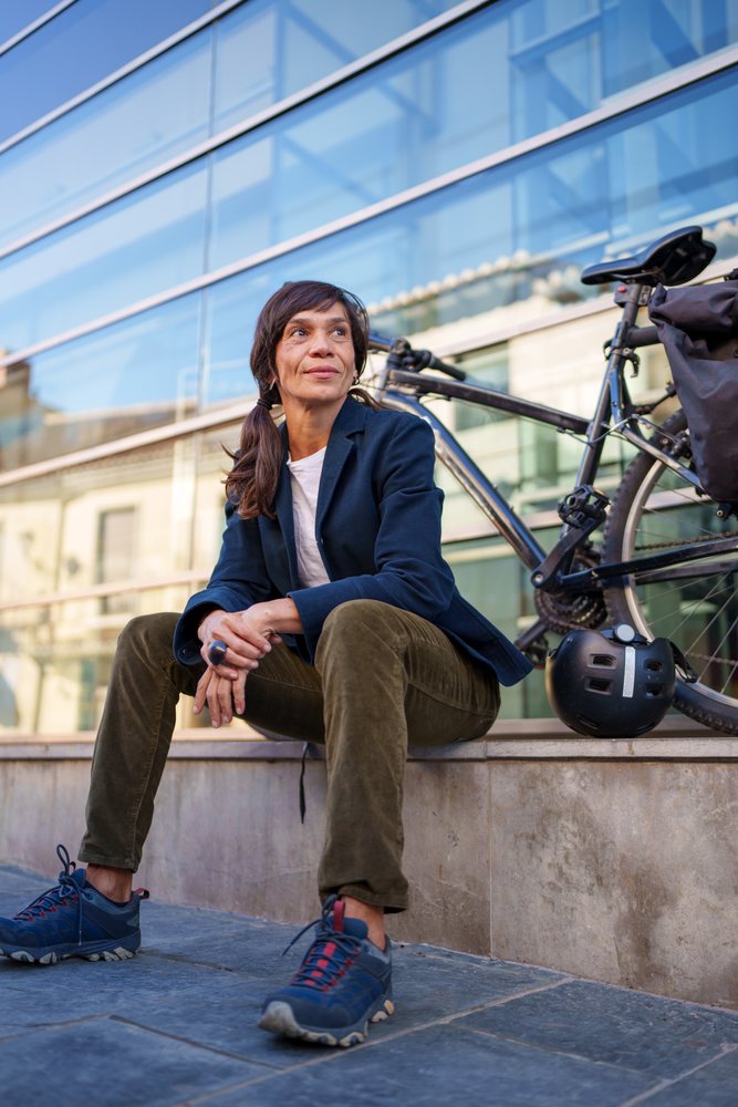 Hispanic woman sitting by bicycle outside modern building