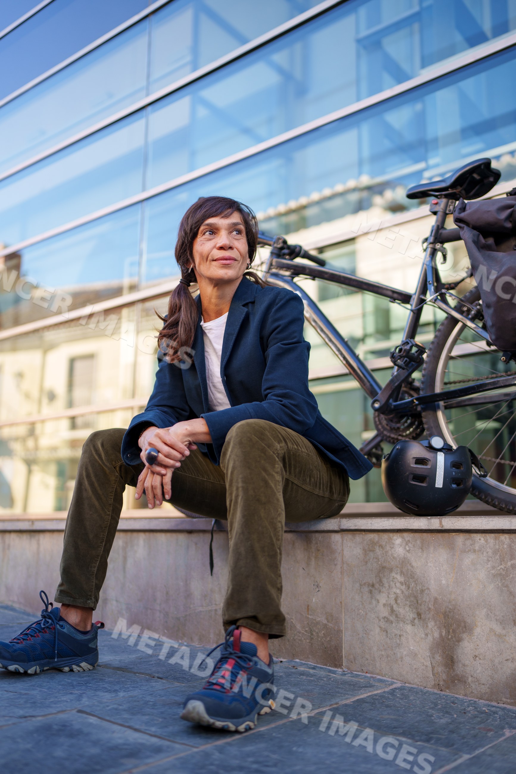Hispanic woman sitting by bicycle outside modern building