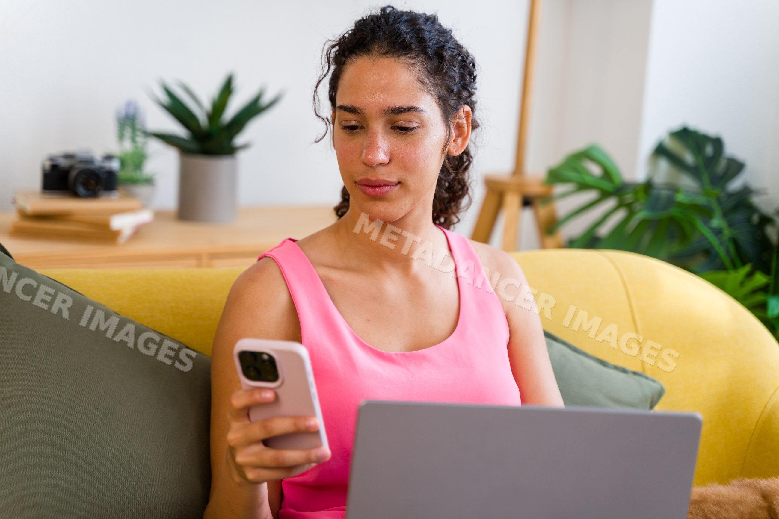 A Hispanic woman multitasks using phone and laptop at home in Spain