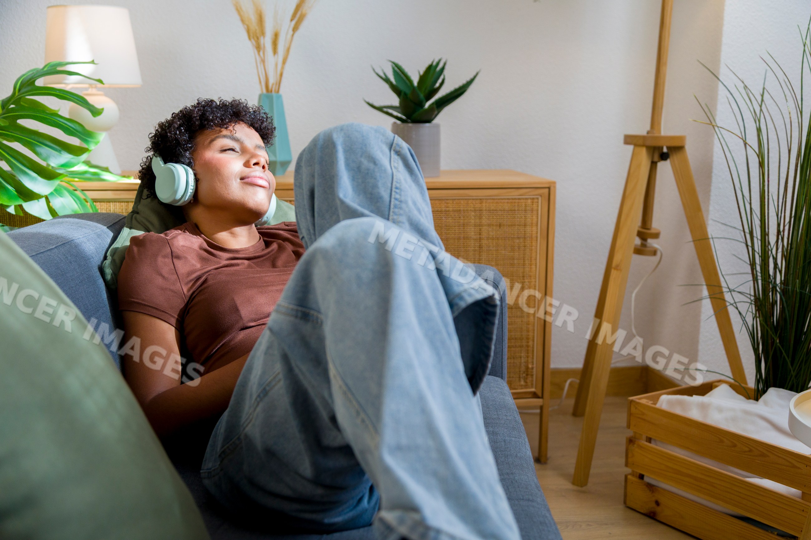 Young African American woman relaxing and listening to music on sofa