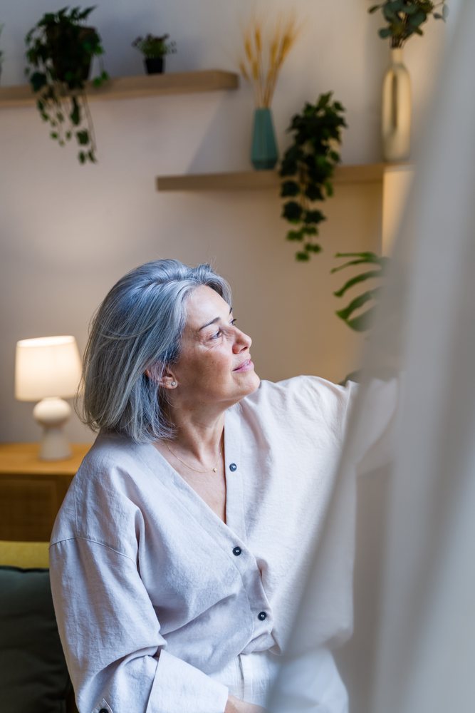 White woman with gray hair sitting contemplatively in living room