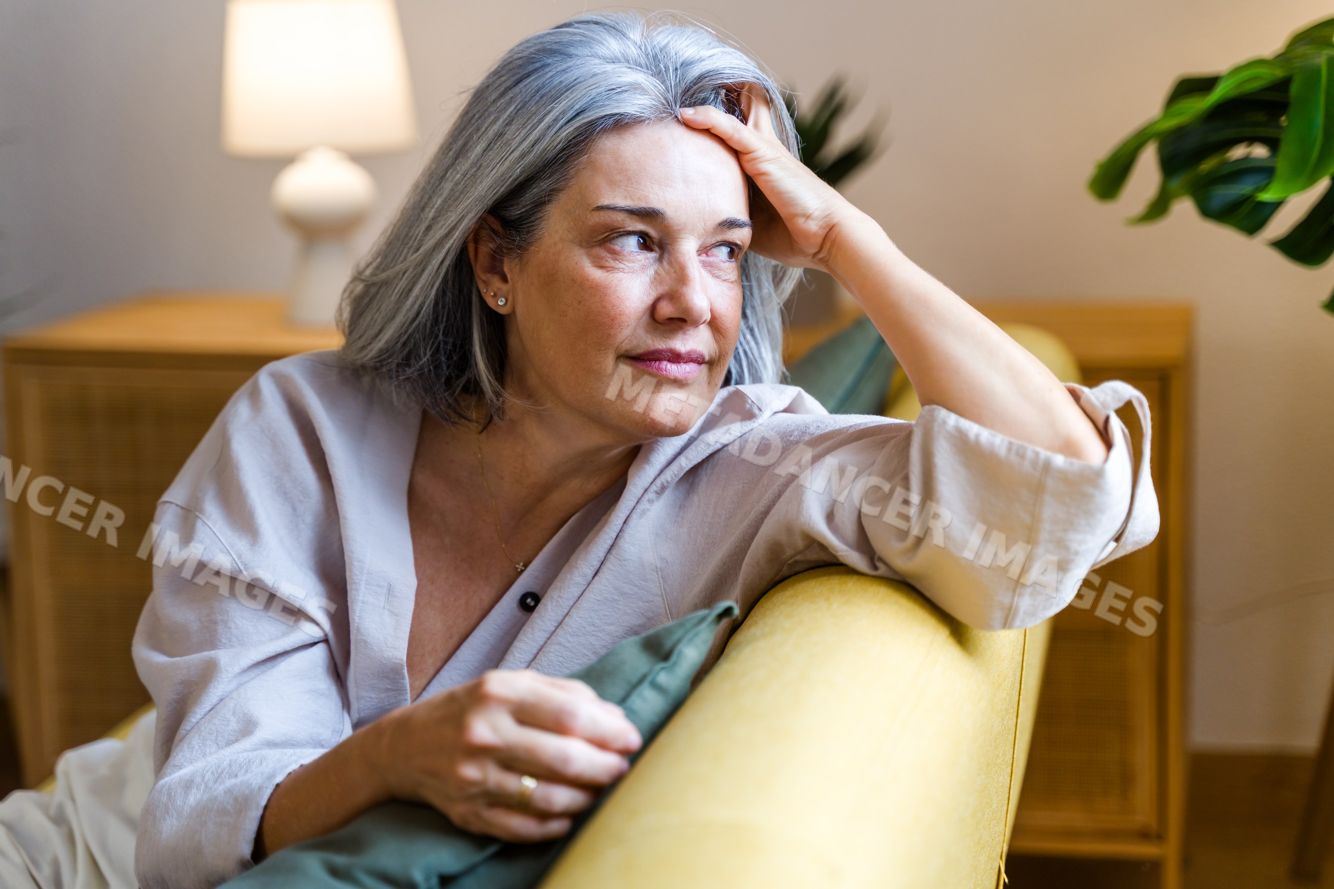 Middle-aged white woman sitting thoughtfully on yellow couch indoors