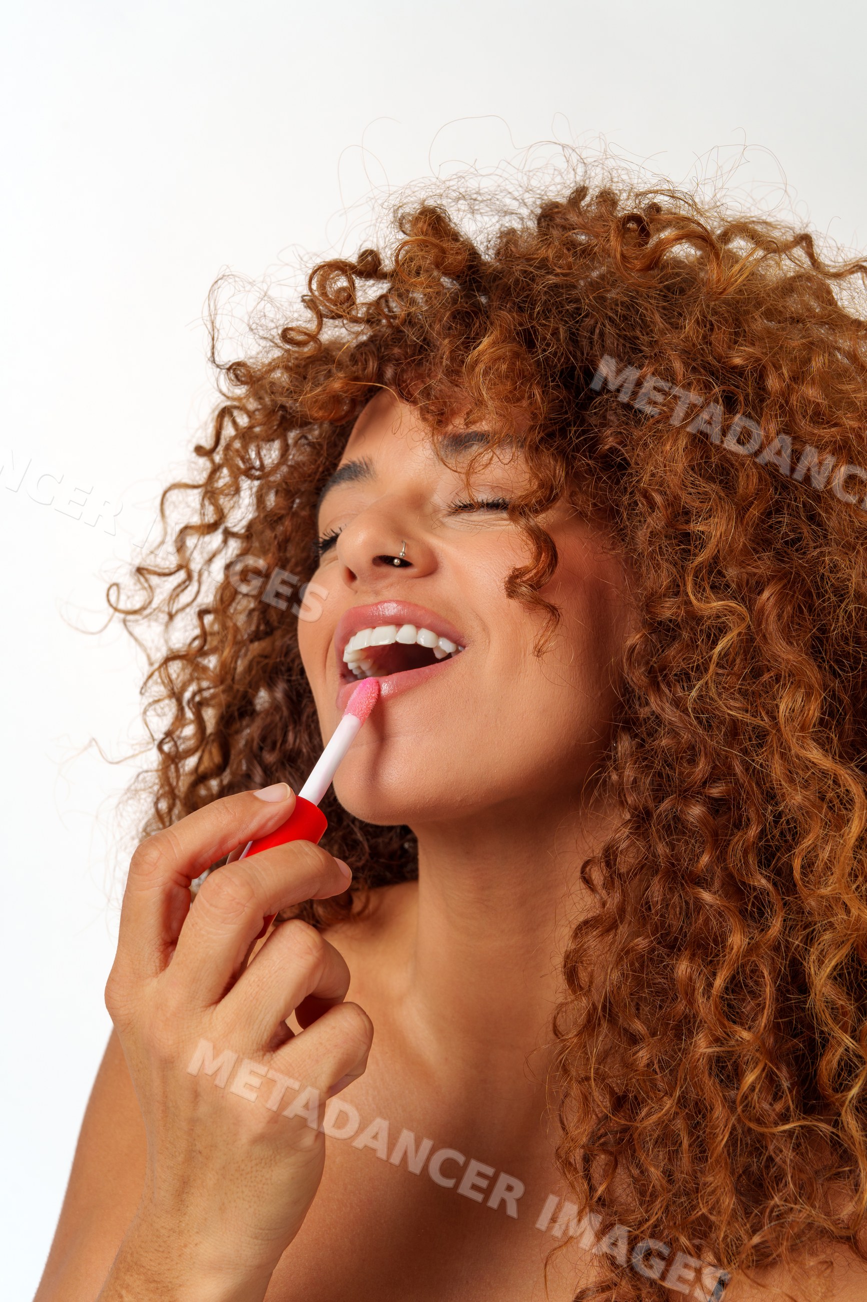 Hispanic woman applying red lip gloss with curly hair