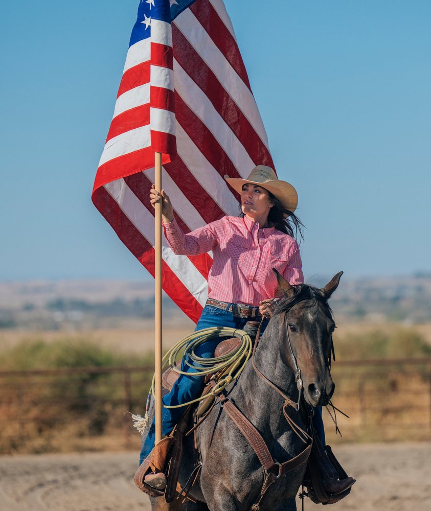 White woman on horse holding american flag in Southwest USA ranch