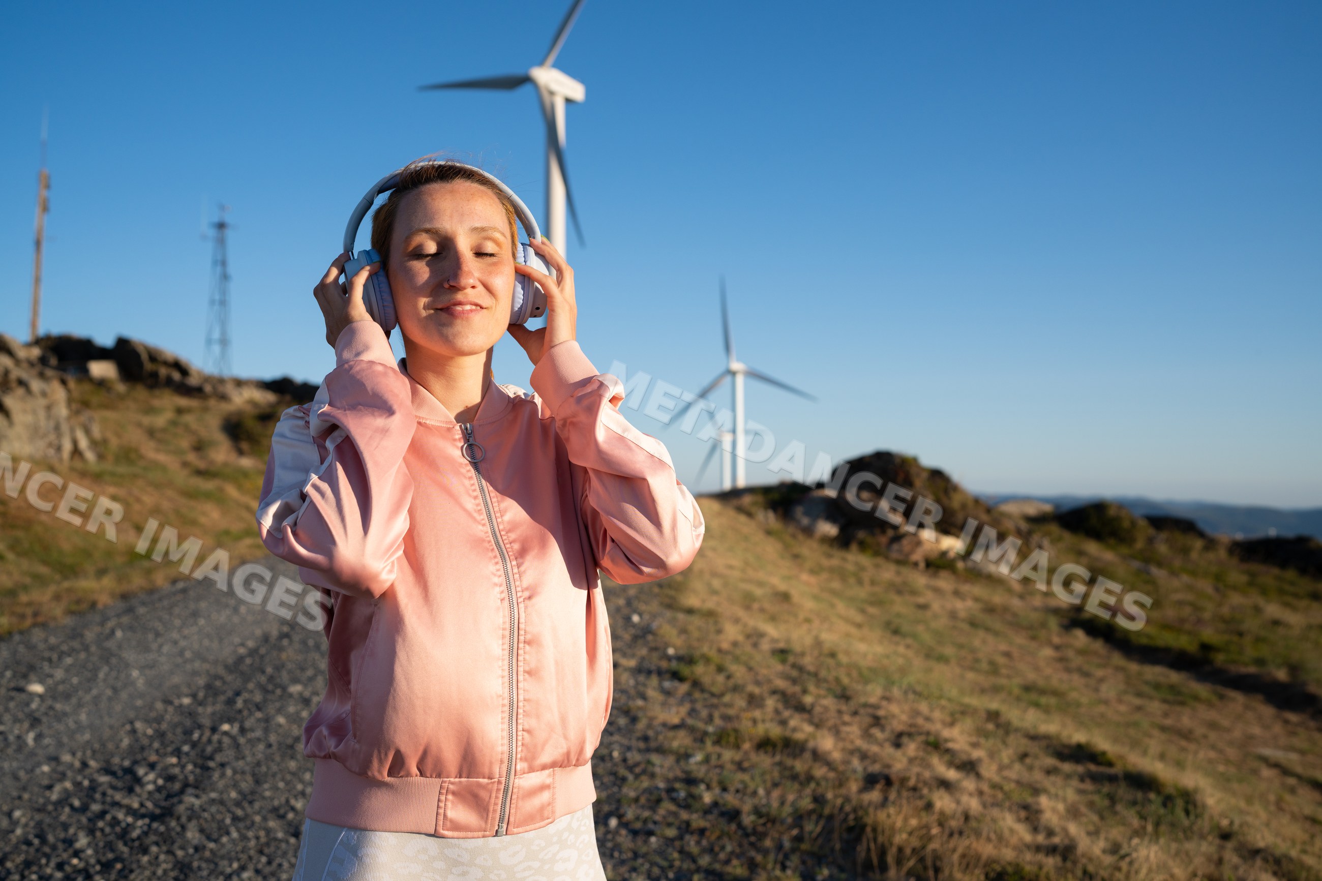 A white woman listens to music near wind turbines in Galicia, Spain