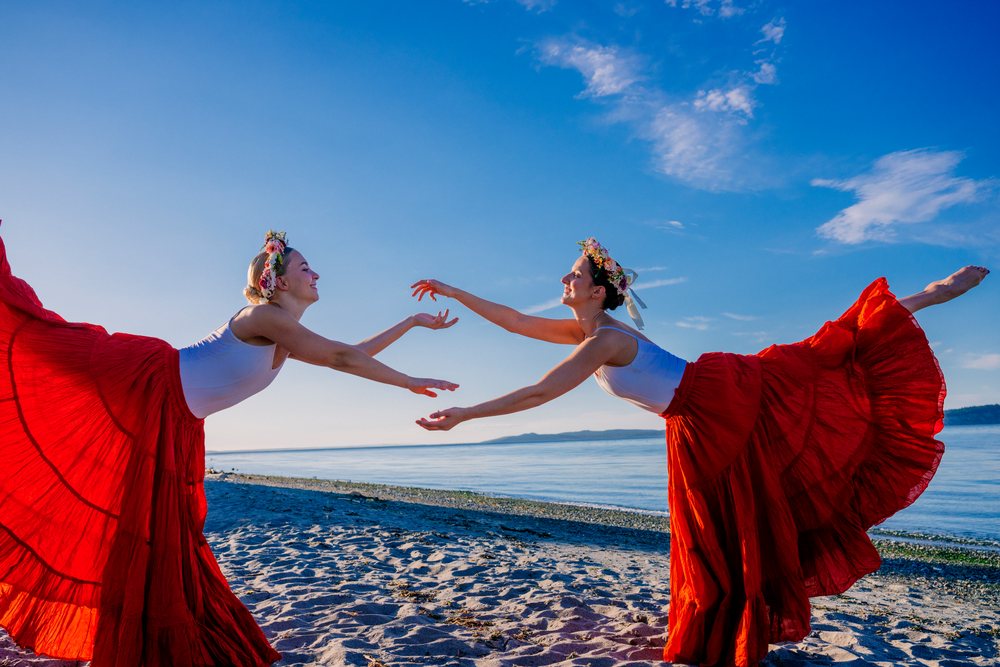 Two white women practice partner acrobatics yoga on a beach in WA, USA