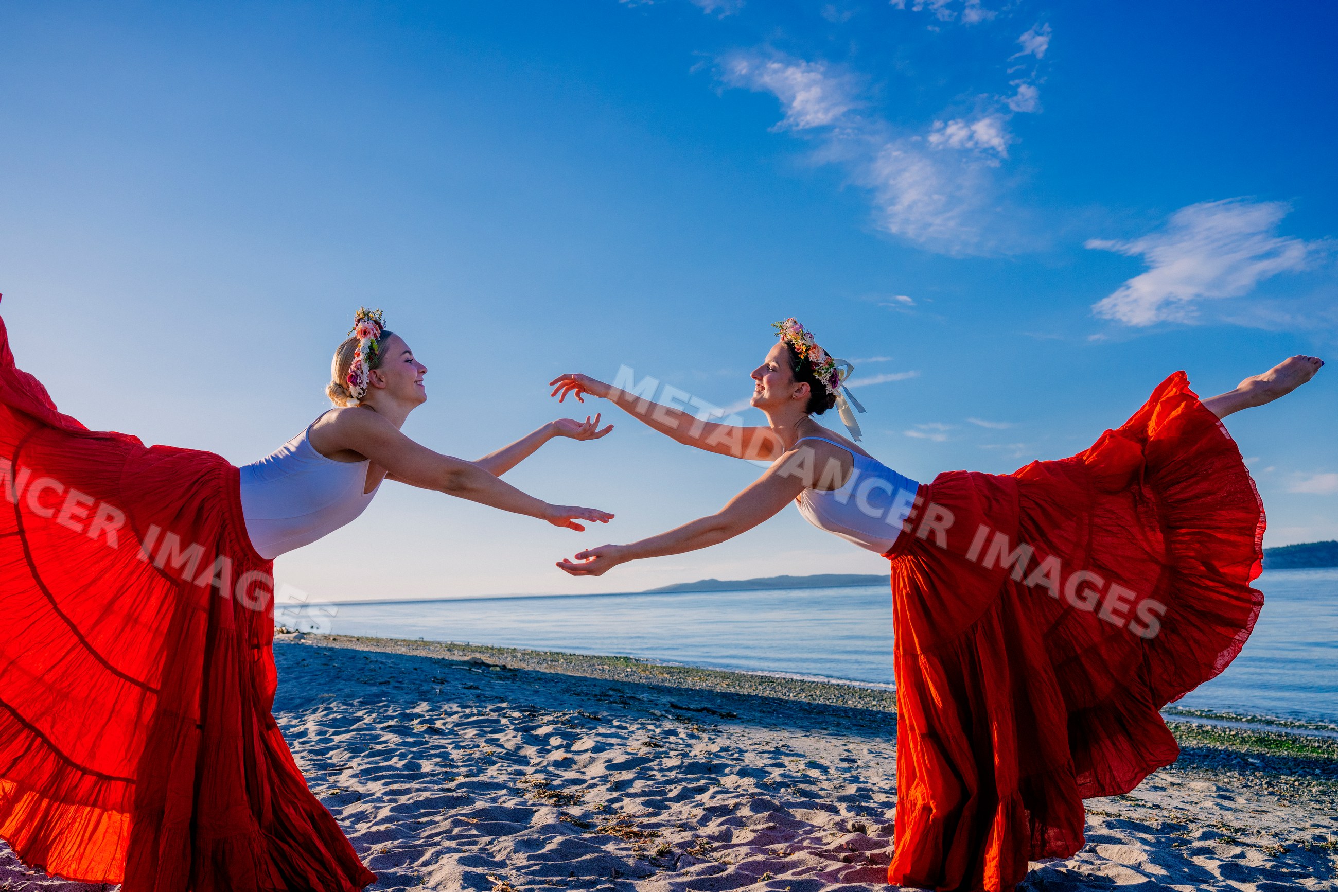 Two white women practice partner acrobatics yoga on a beach in WA, USA