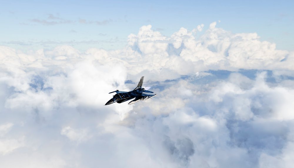 A fighter jet flies high above the clouds in a clear blue sky