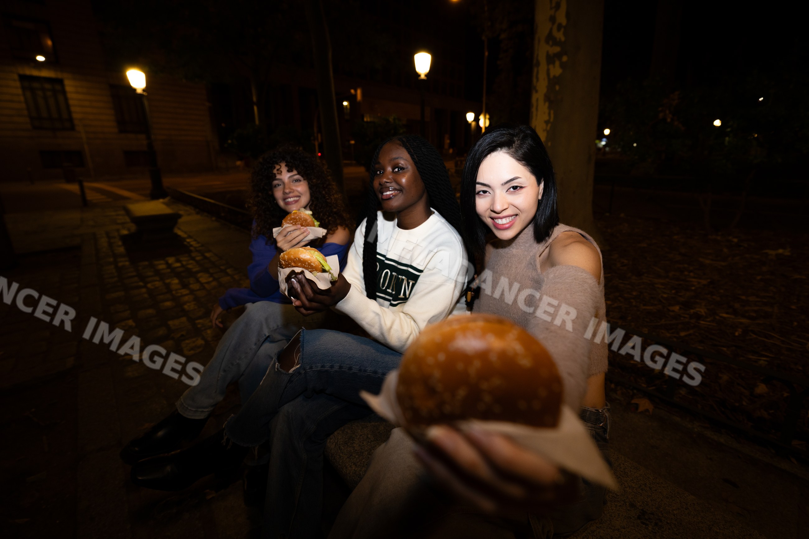 Three friends enjoying hamburgers sitting in a park at night