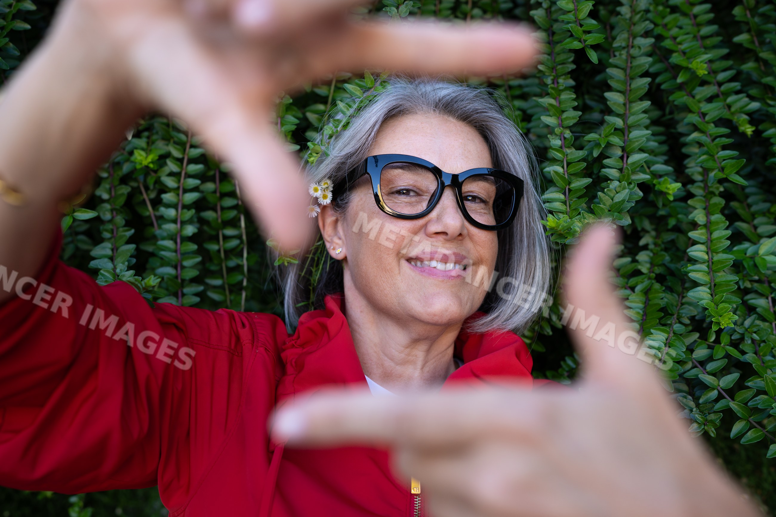 White woman with gray hair framing view with hands outdoors