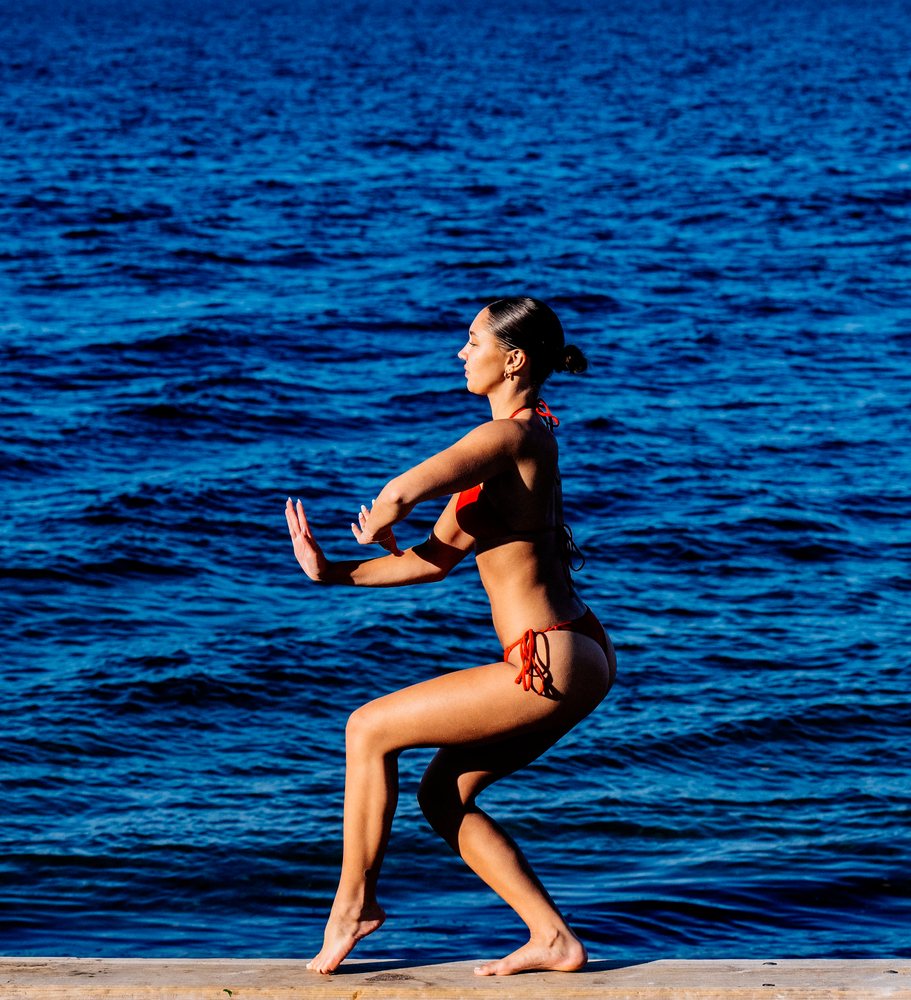 Woman in red swimsuit doing squat exercise by the water in washington