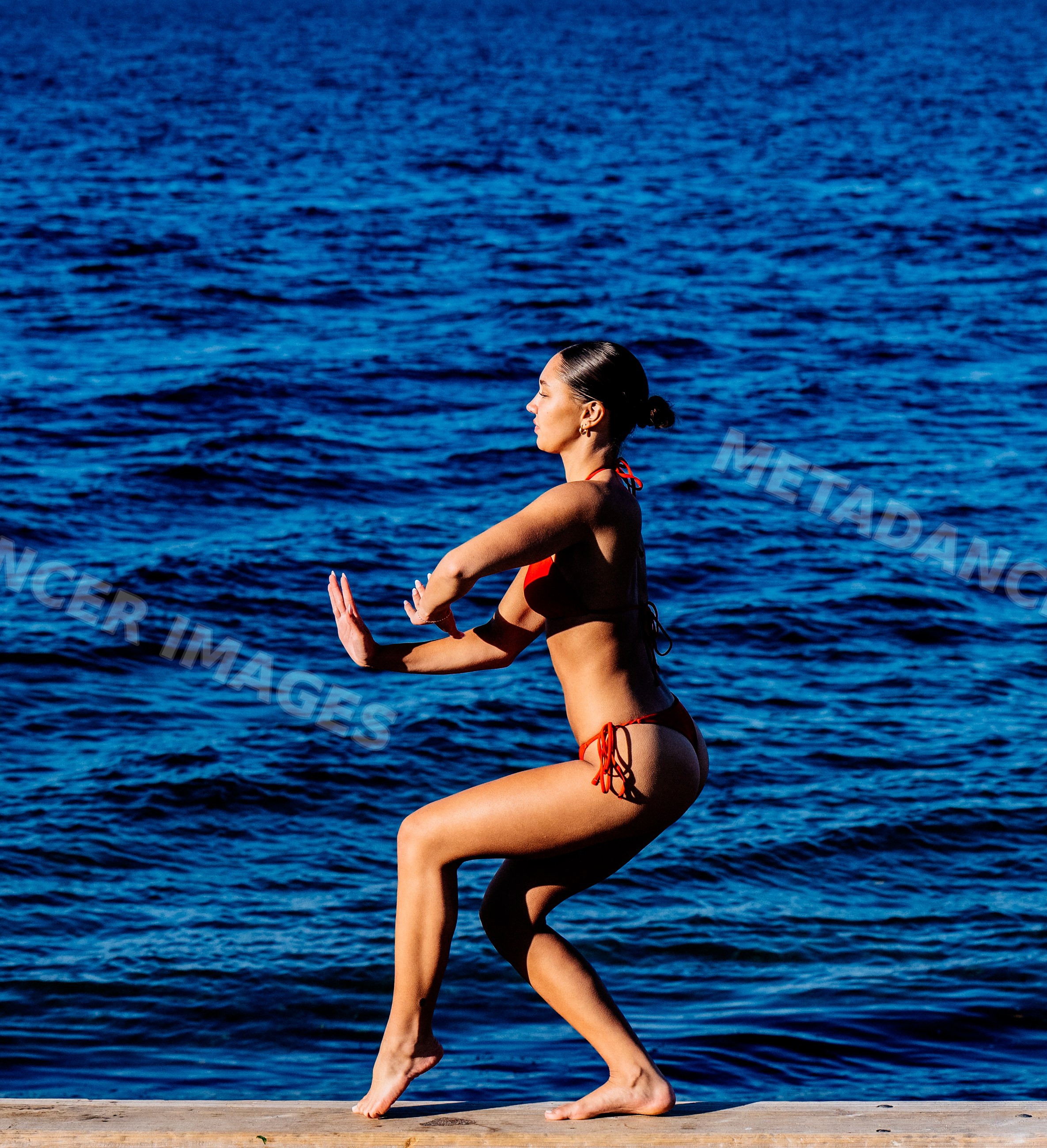 Woman in red swimsuit doing squat exercise by the water in washington