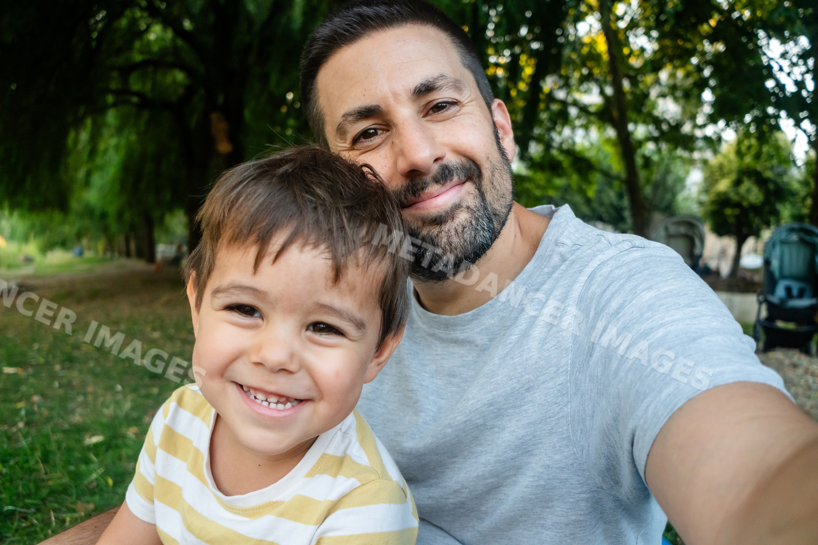 Father and son happily take a selfie together outdoors in a park