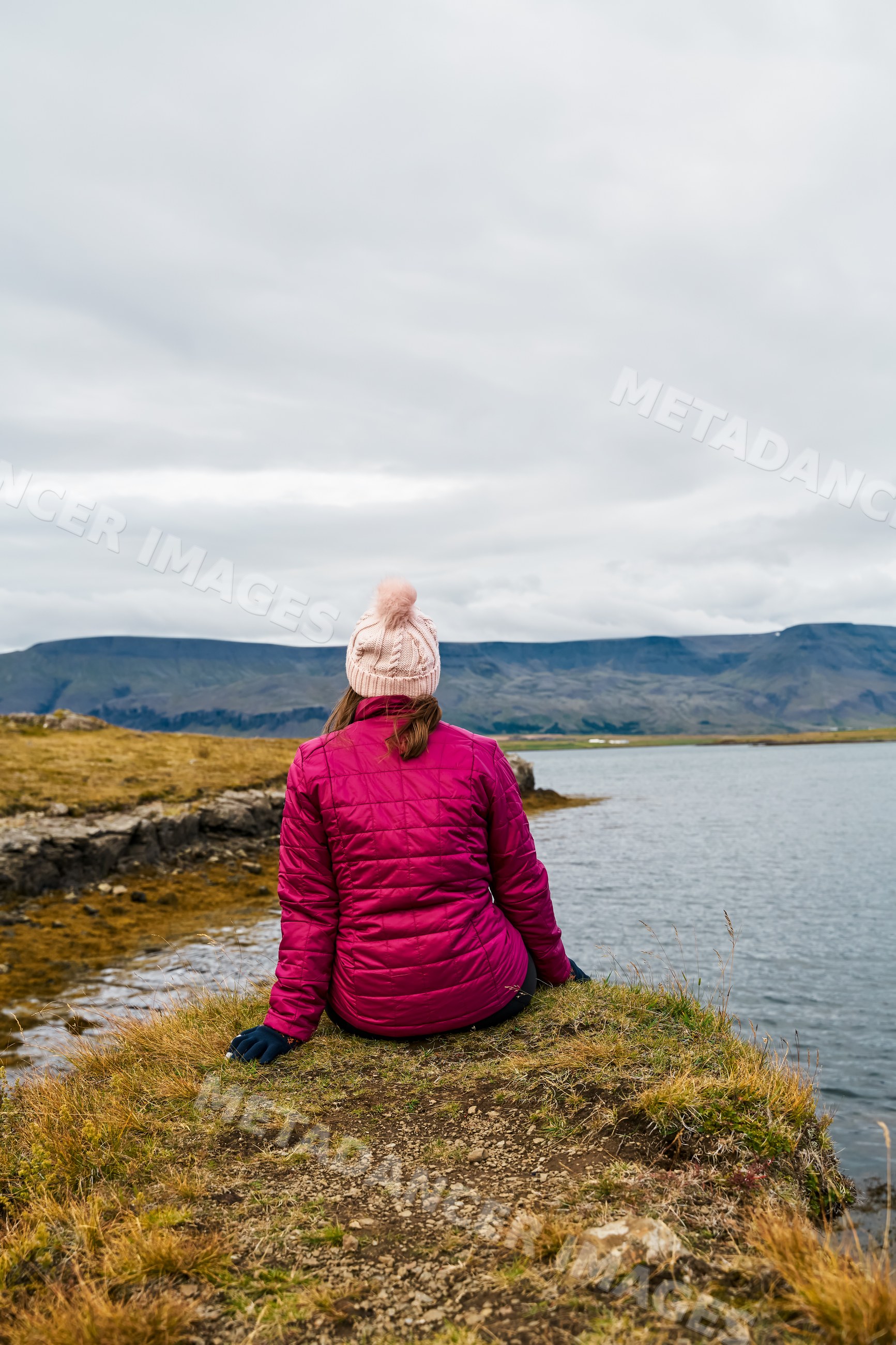 A white woman sits by a lake enjoying the natural scenery