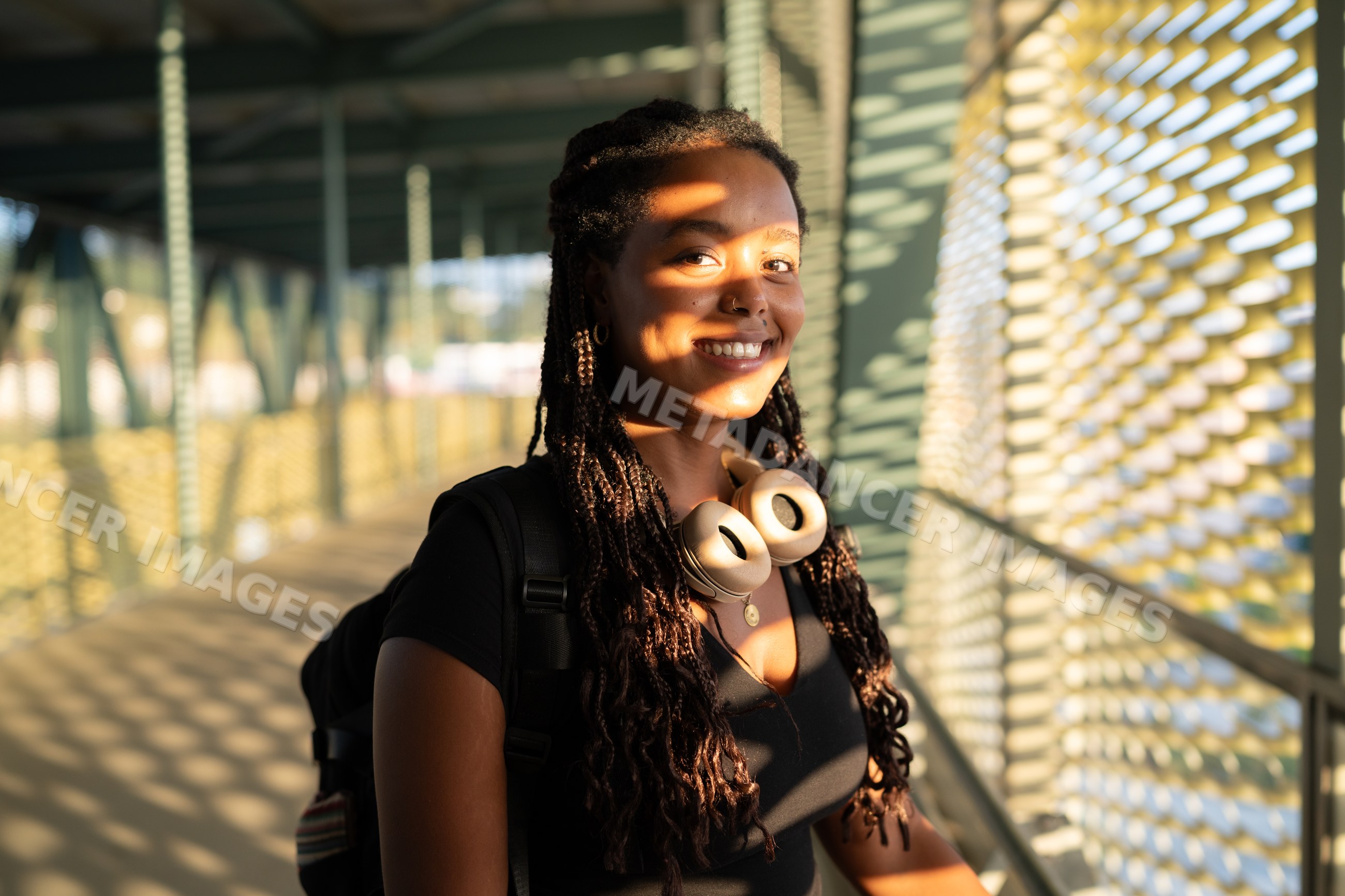 A young African American woman with headphones smiles on urban walkway