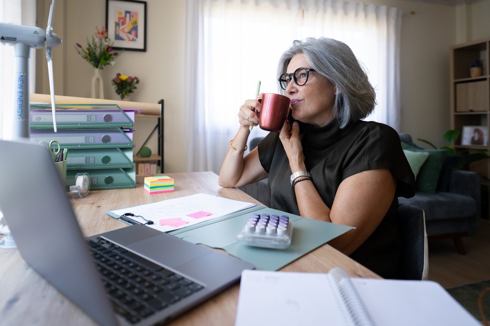 White woman drinking coffee at home office desk in a office