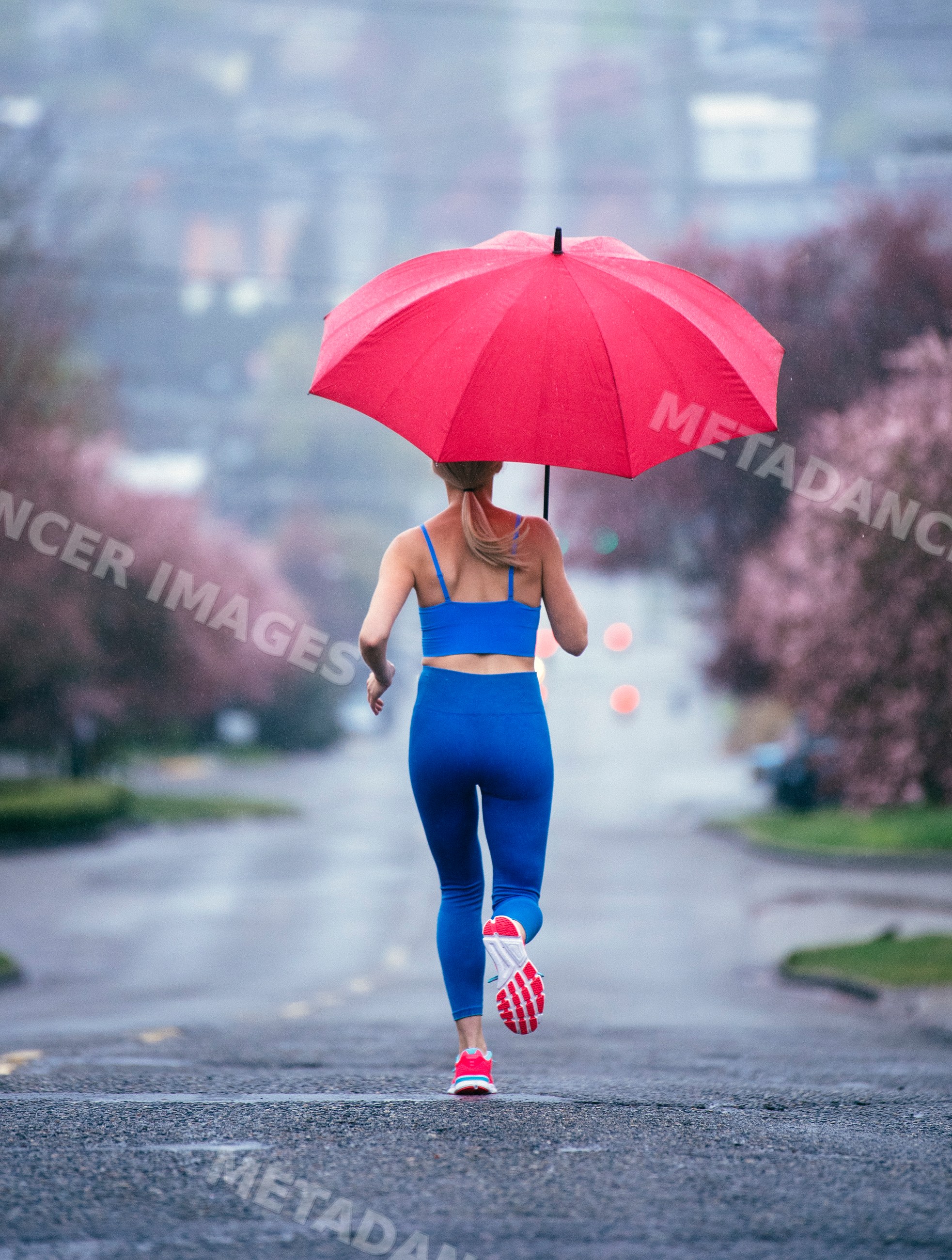 White woman running with red umbrella on rainy urban street