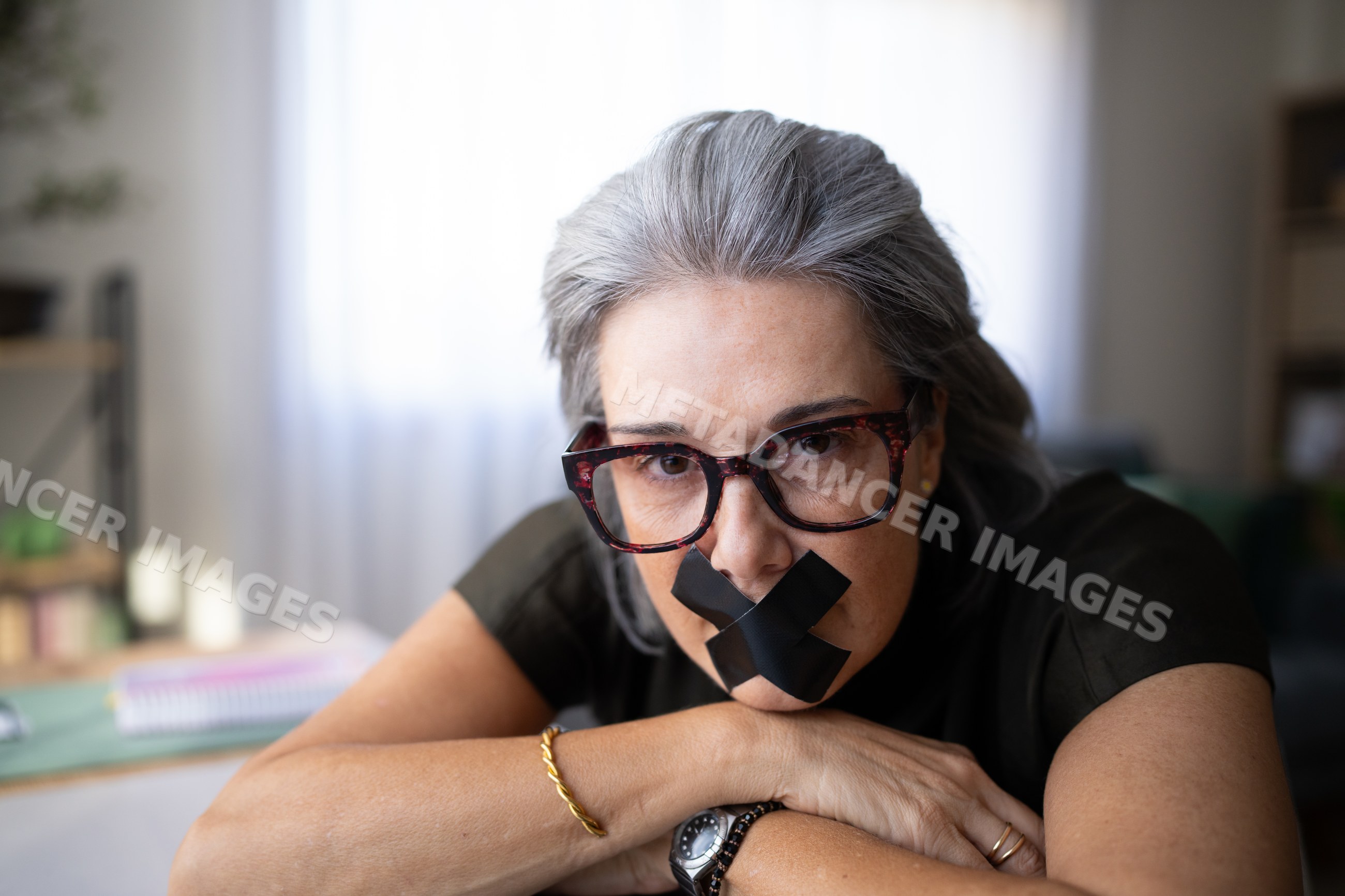 Older white woman with black tape on mouth resting arms indoors