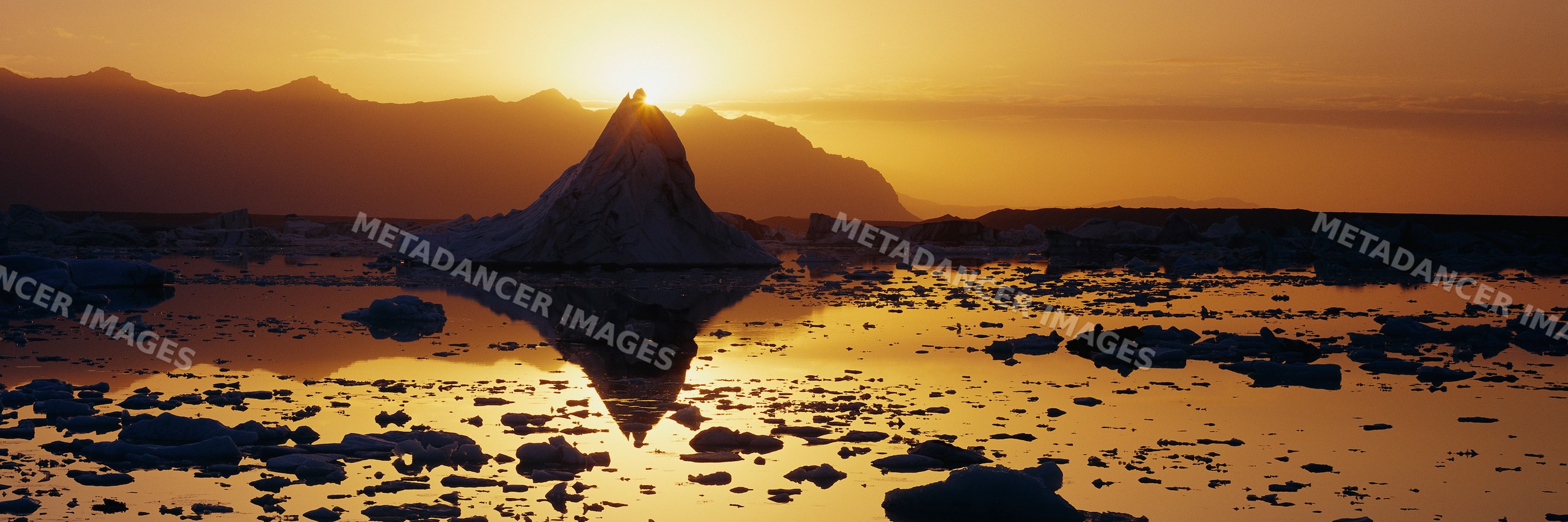 Iceberg reflection at sunset with mountainous arctic landscape
