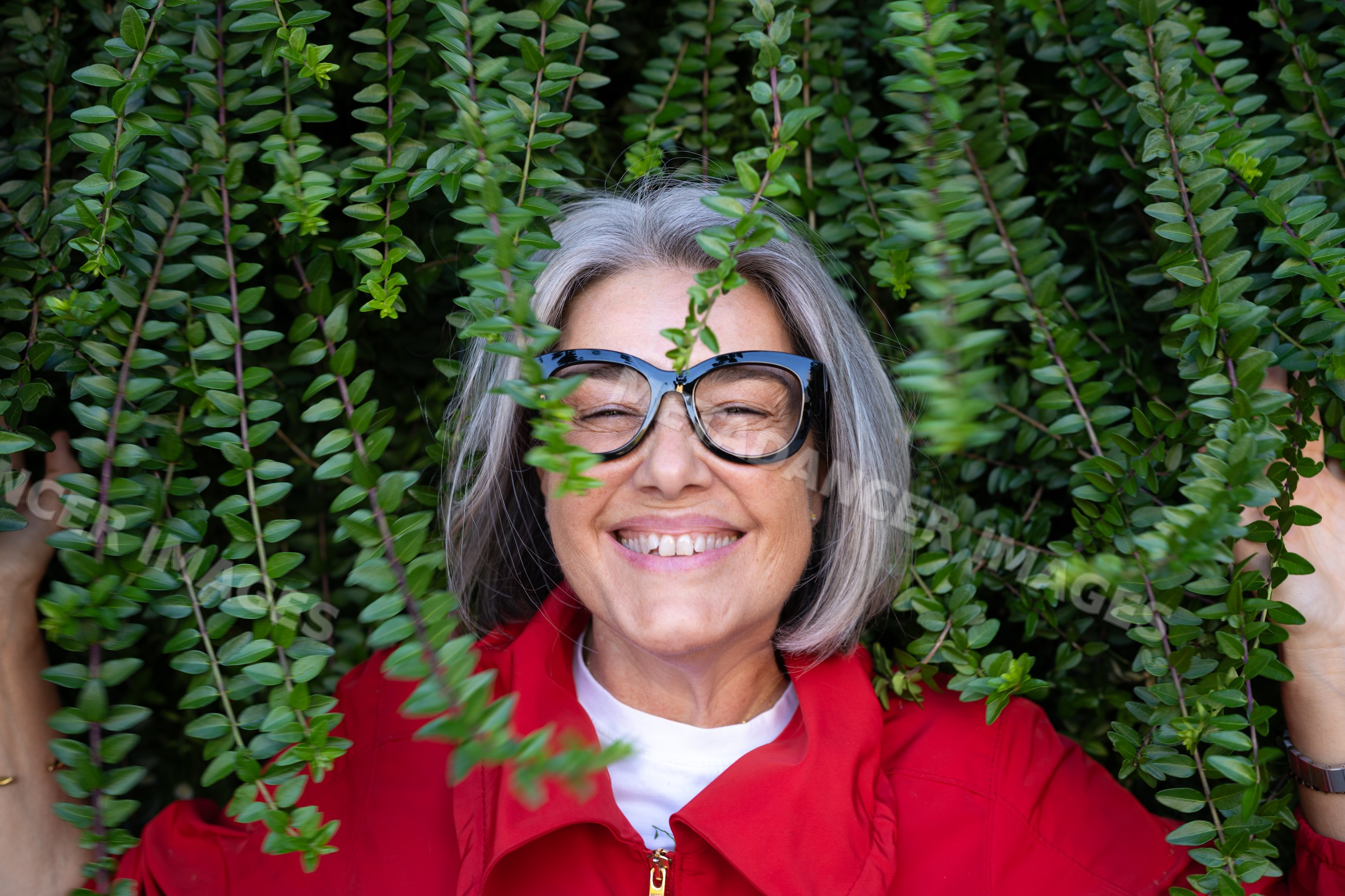 Smiling white woman with gray hair among green leaves outdoors