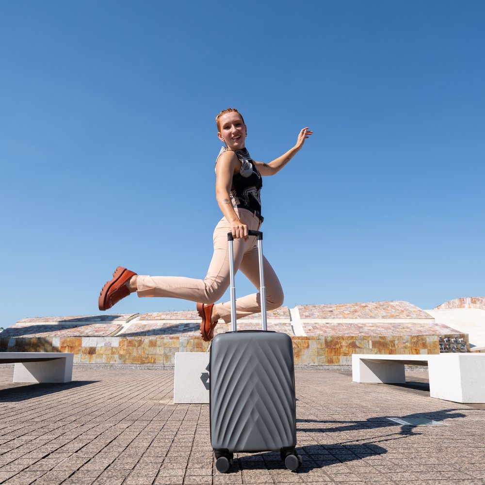 White woman jumping with suitcase in outdoor urban plaza