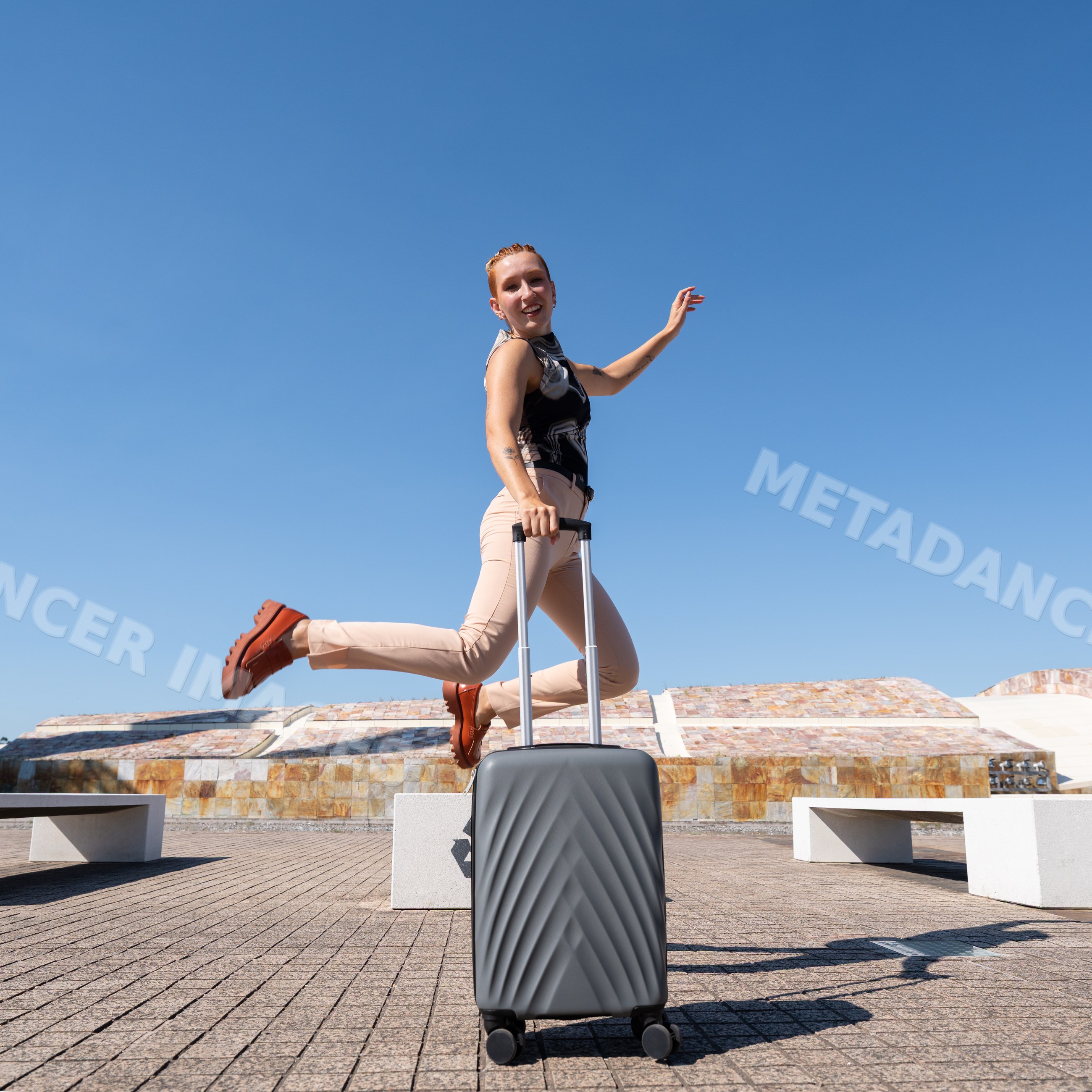 White woman jumping with suitcase in outdoor urban plaza